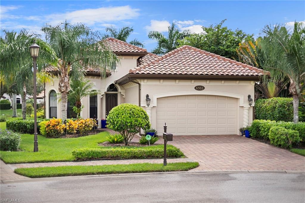 Stucco home with a red tile roof, two-car garage, palm trees, and landscaped lawn.
