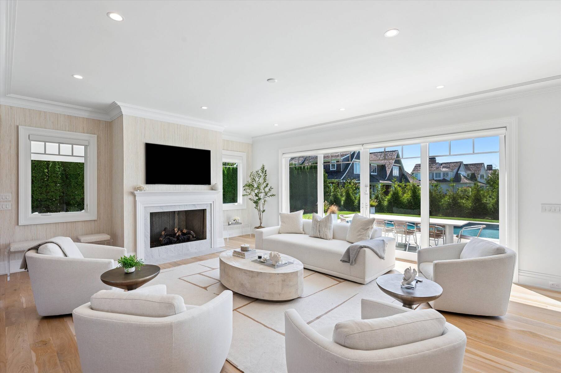 Bright living room with a marble fireplace and wide glass doors overlooking a patio pool.