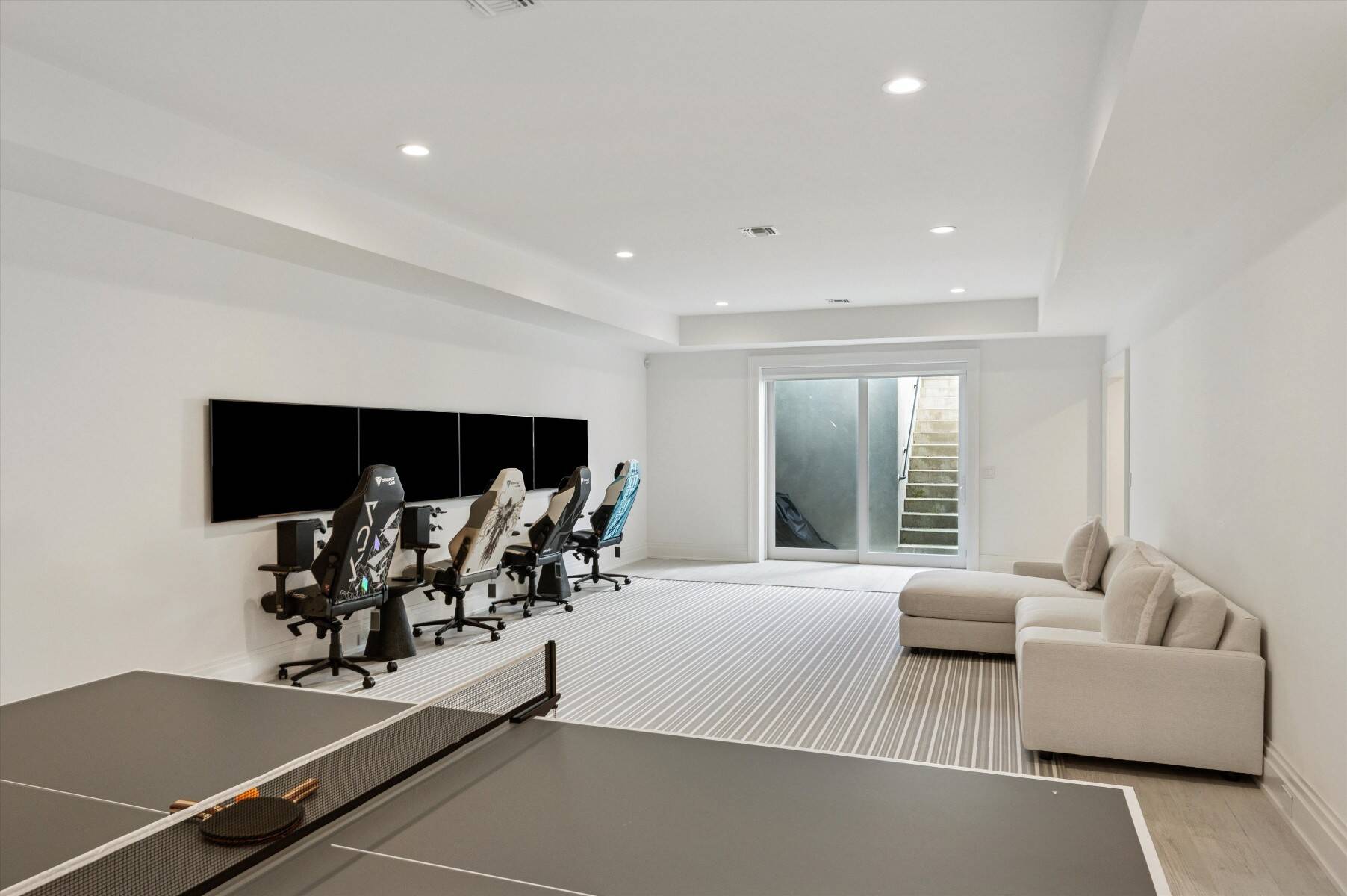 Recreation room with a ping-pong table, gaming stations, and a sectional sofa.