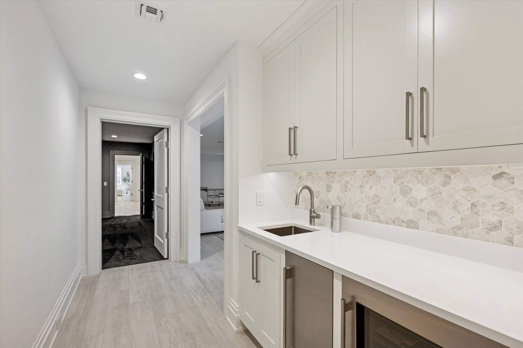 Modern wet bar with white cabinetry, hexagonal tile backsplash, sink, and under-counter beverage refrigerators.