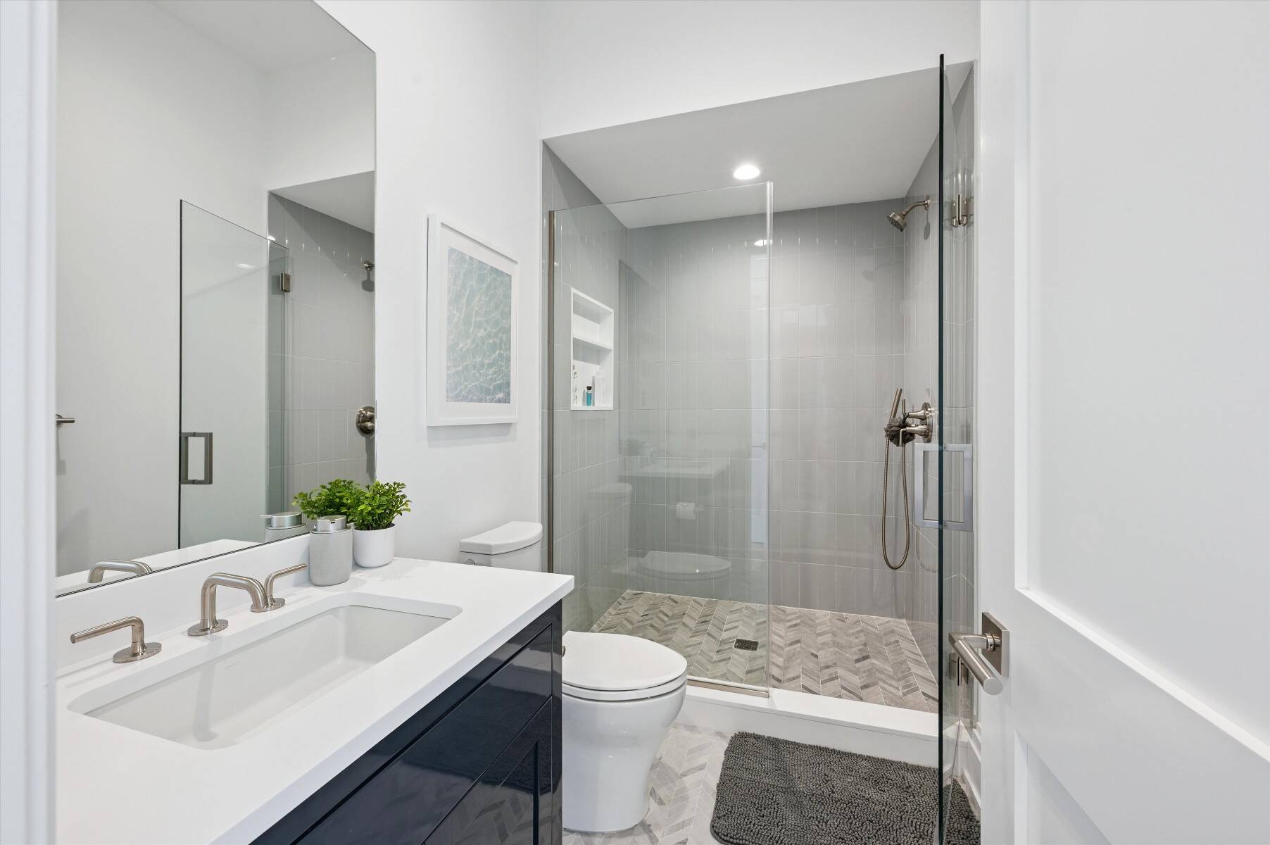 Modern bathroom with a glass walk-in shower, herringbone tile floor, and dark vanity.
