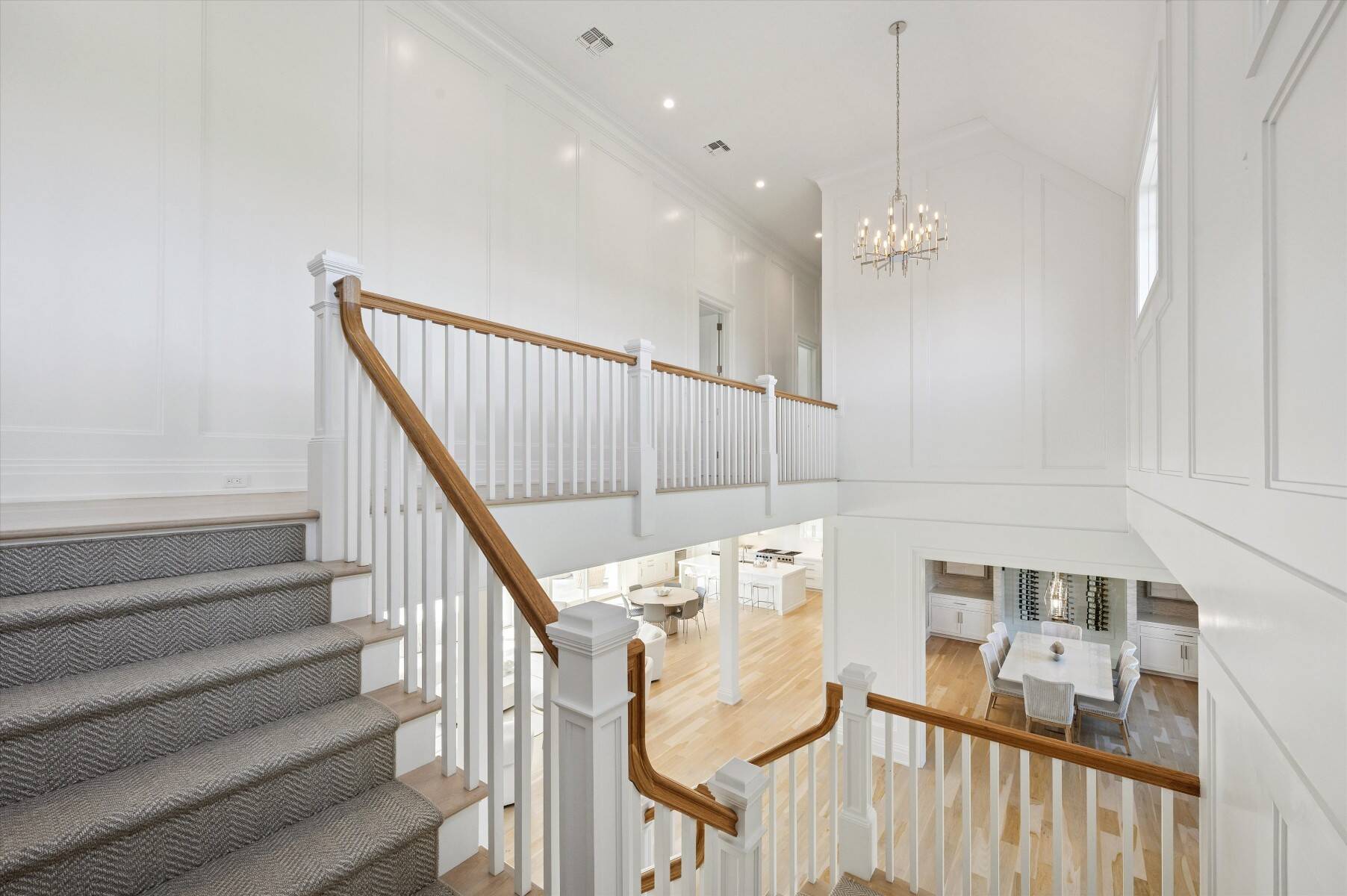 Bright stair hall with carpeted stairs, wood handrails, a chandelier, and dining areas below.