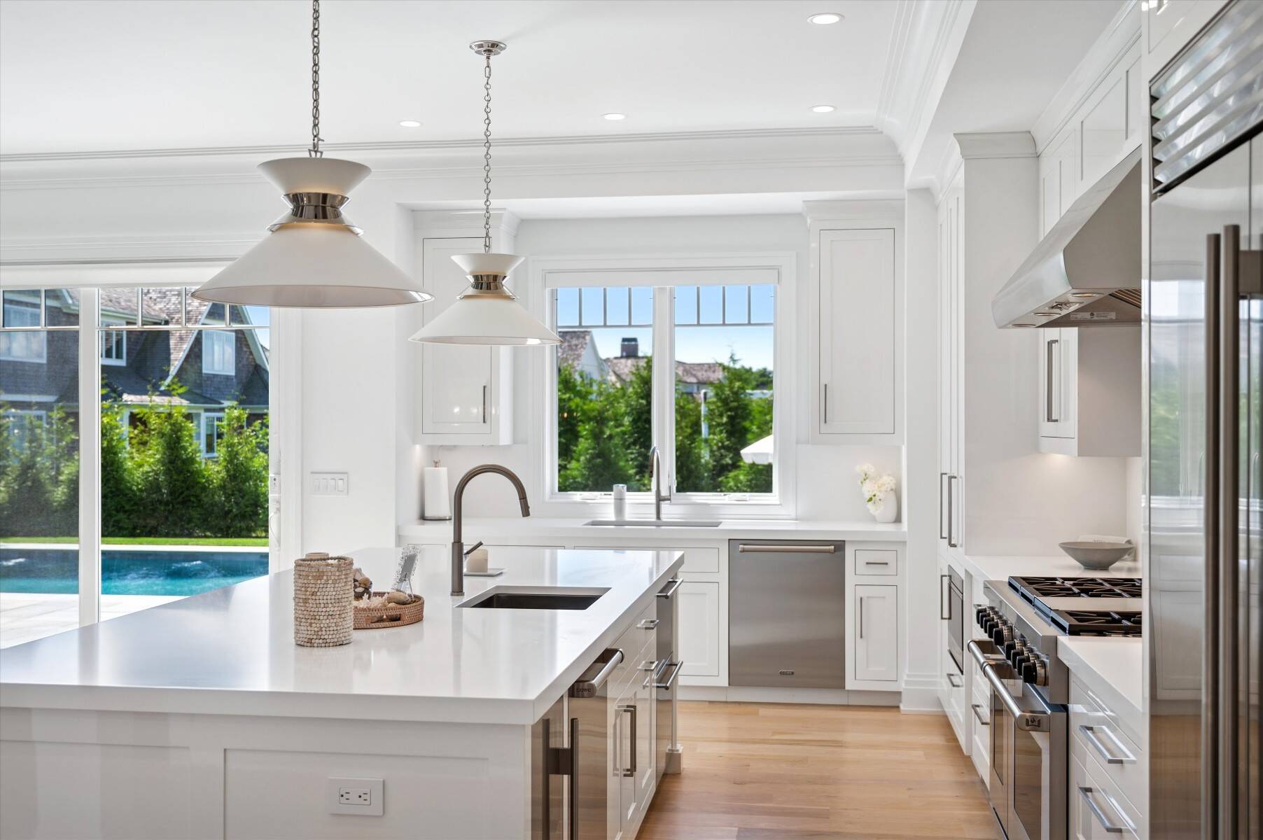 Bright white kitchen with a large island, stainless appliances, and windows overlooking a swimming pool.