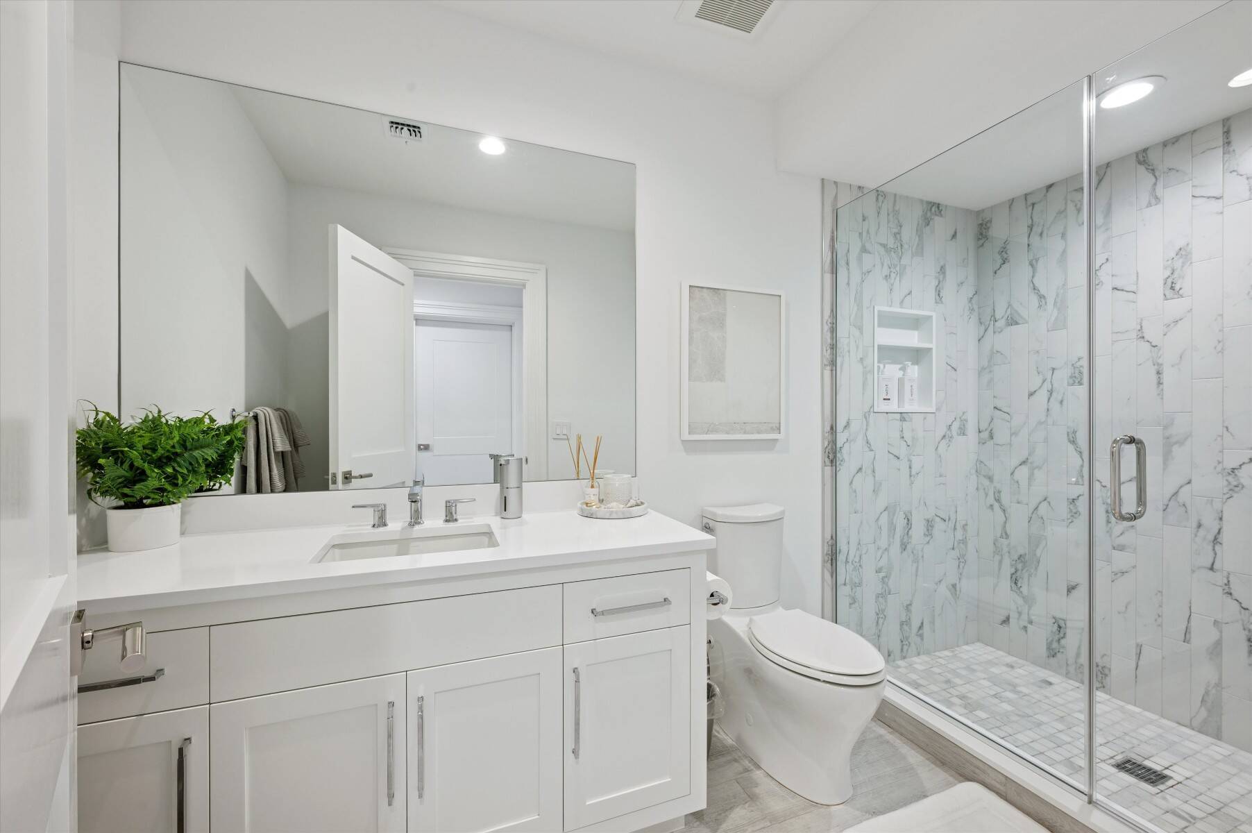 Modern bathroom with a white vanity and glass shower lined in marble-look tile.