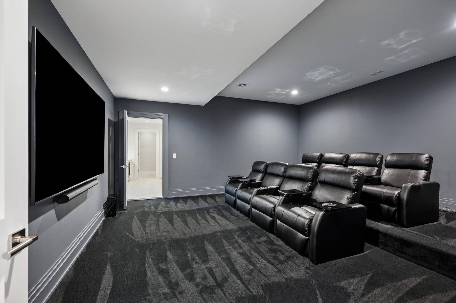 Home theater with tiered black leather recliners and a large wall-mounted screen.