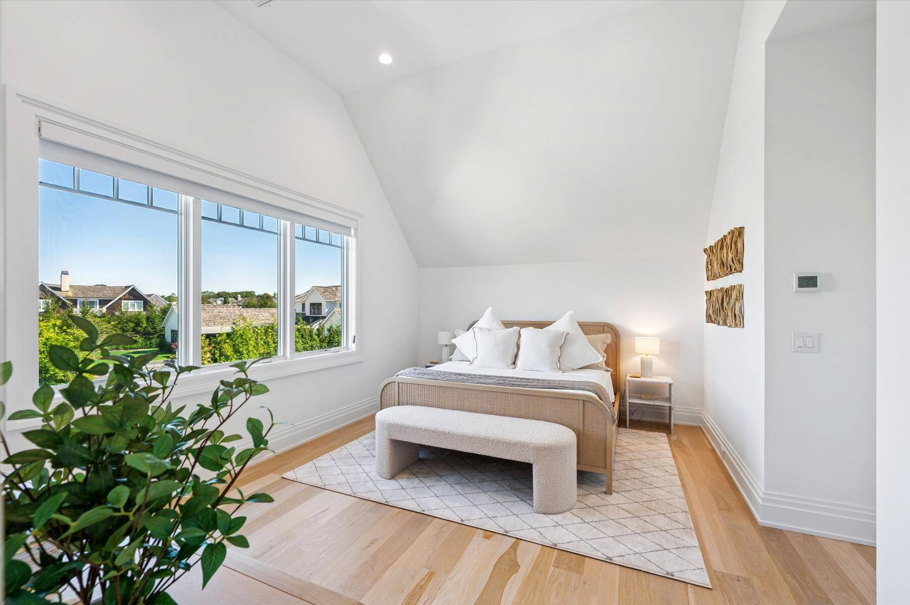 Staged bedroom with a vaulted ceiling, large windows, and a woven bed with white bedding.
