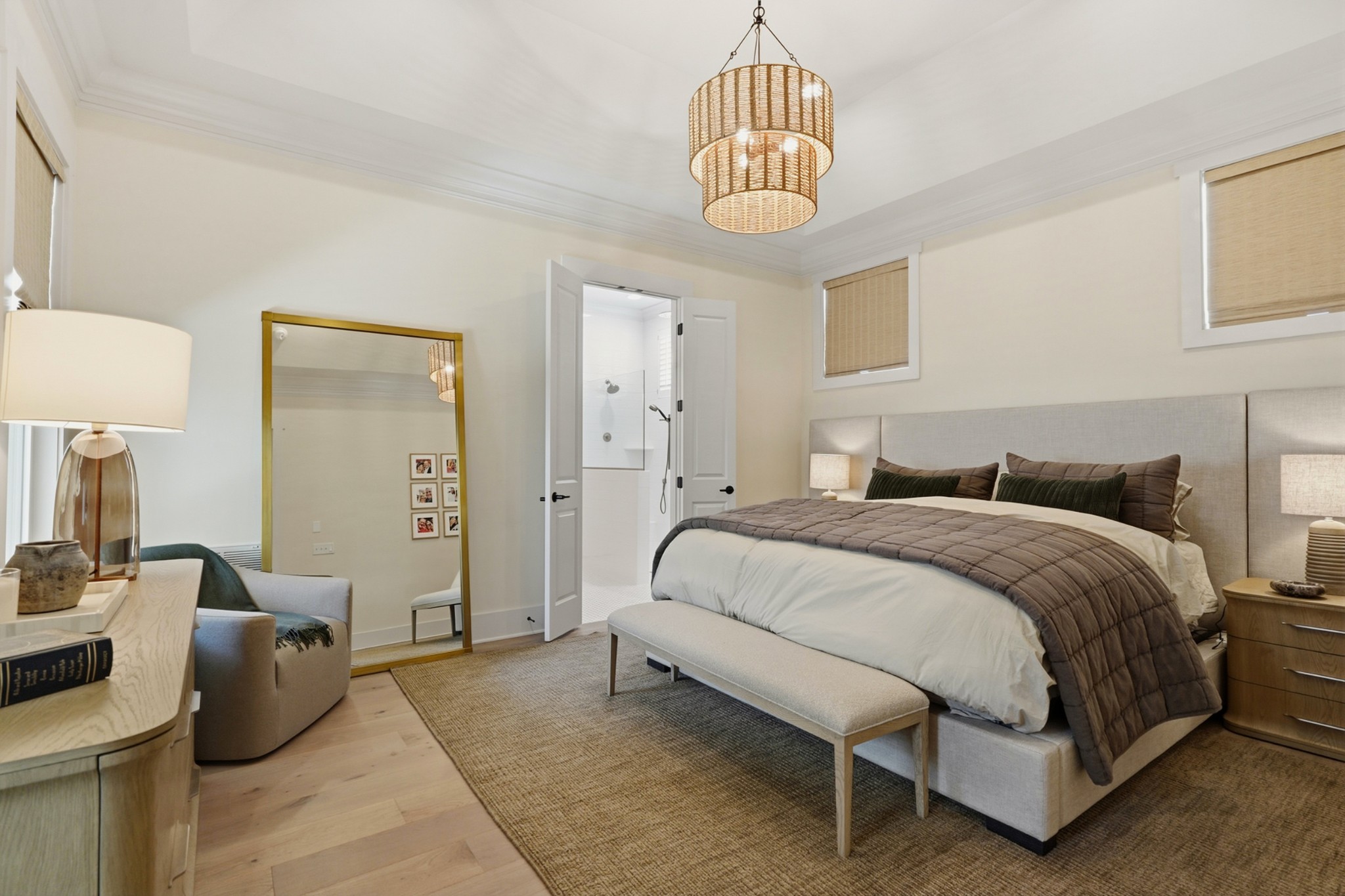 Furnished bedroom with a large upholstered bed, woven pendant light, and open doorway to a bathroom.