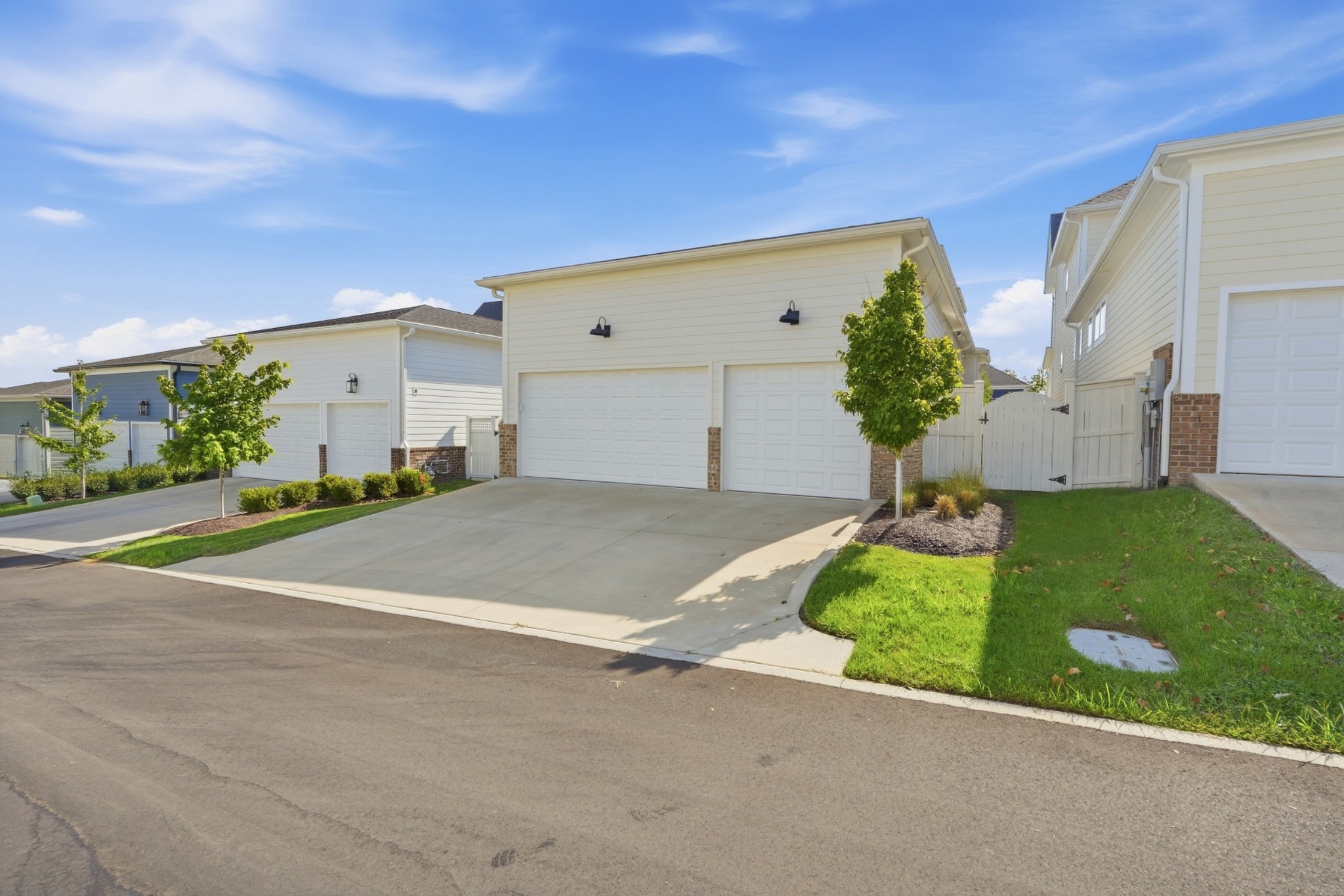 Light-sided home with two garage doors, a wide driveway, and landscaped lawn.