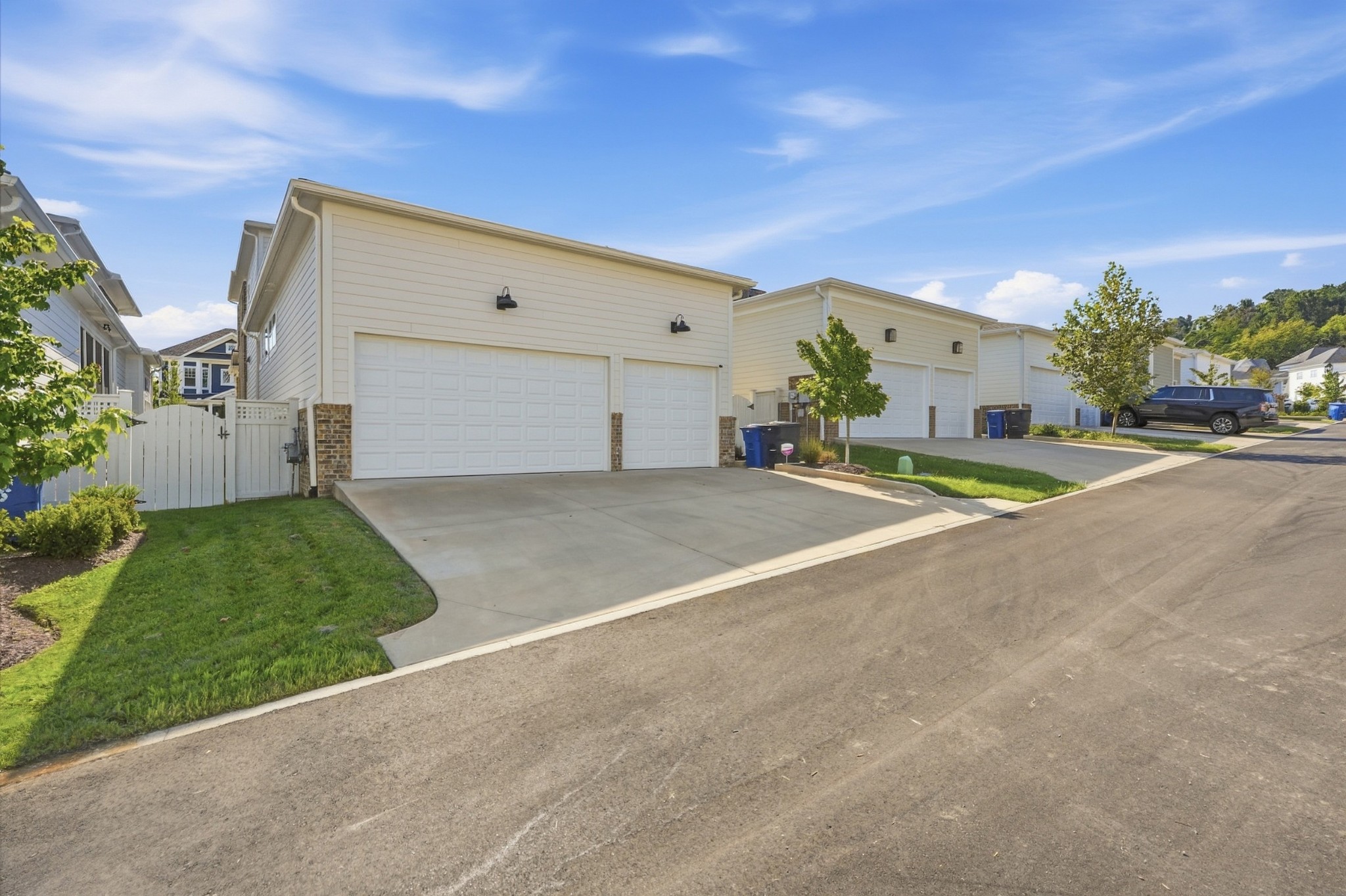 Home exterior with wide driveway, two white garage doors, and a fenced lawn.