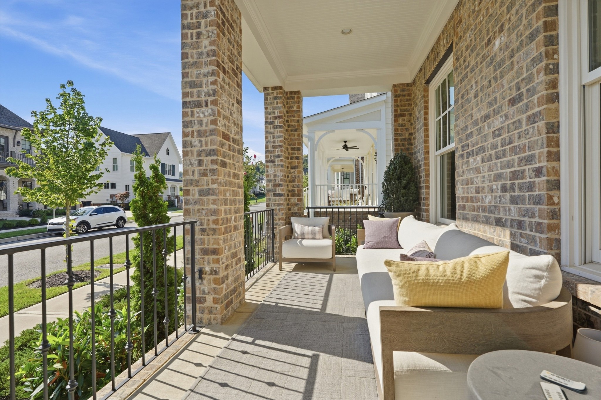 Covered brick porch furnished with a white sofa and chairs, overlooking a leafy residential street.