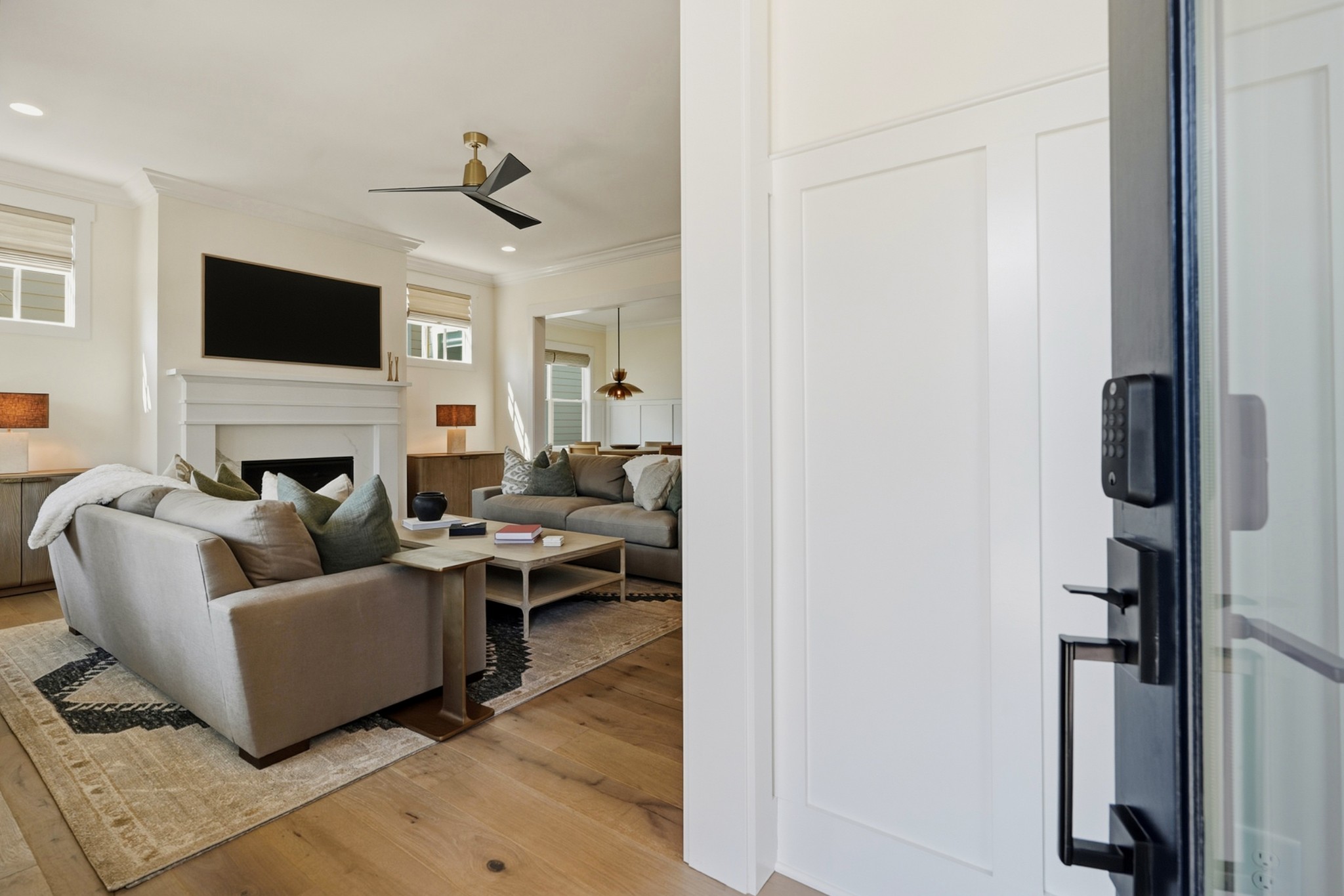 Staged living room with neutral sofas, a fireplace, and wood floors, seen from the open front door.