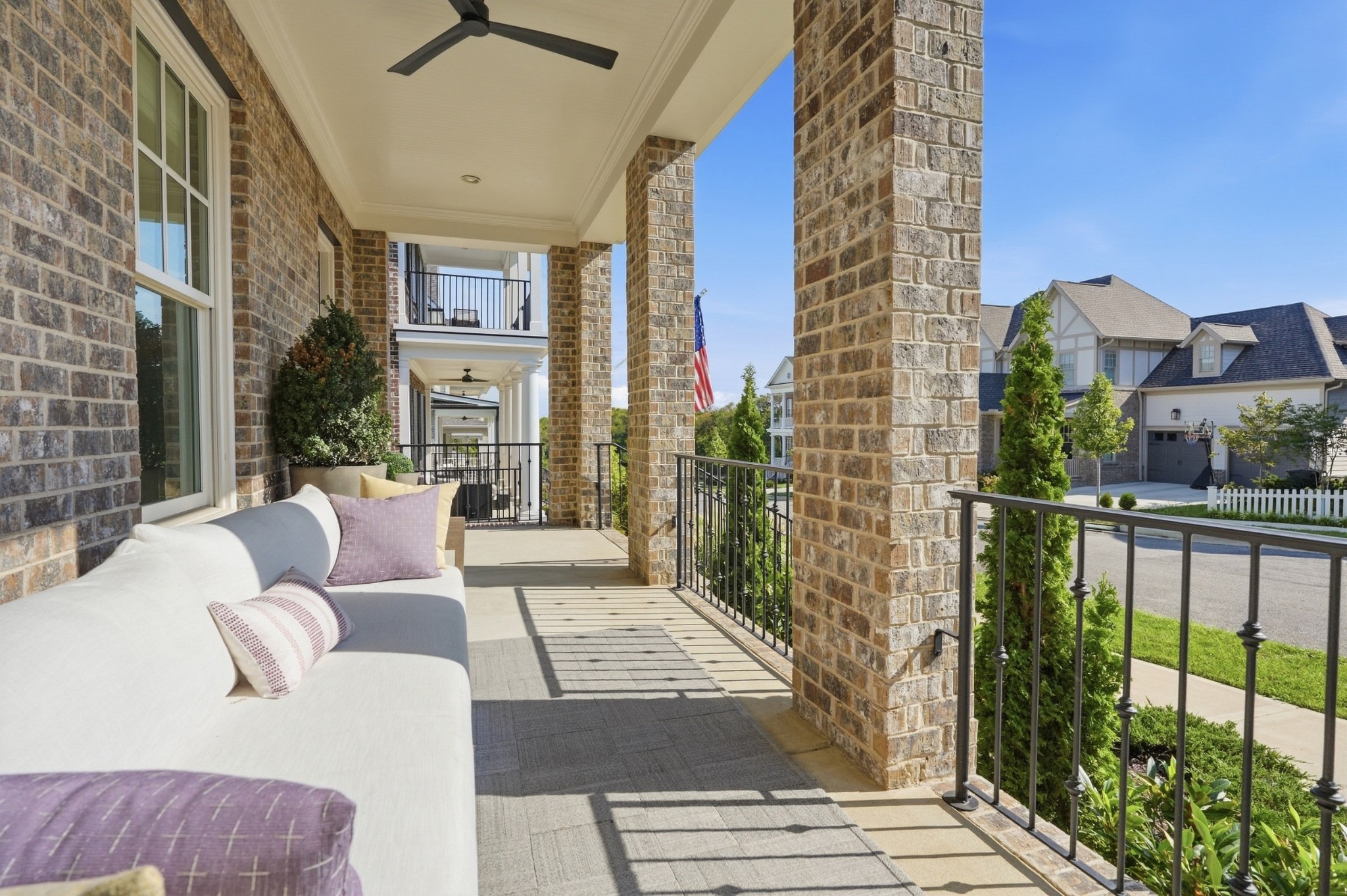 Covered brick porch with a white sofa, ceiling fans, and views of neighboring homes.