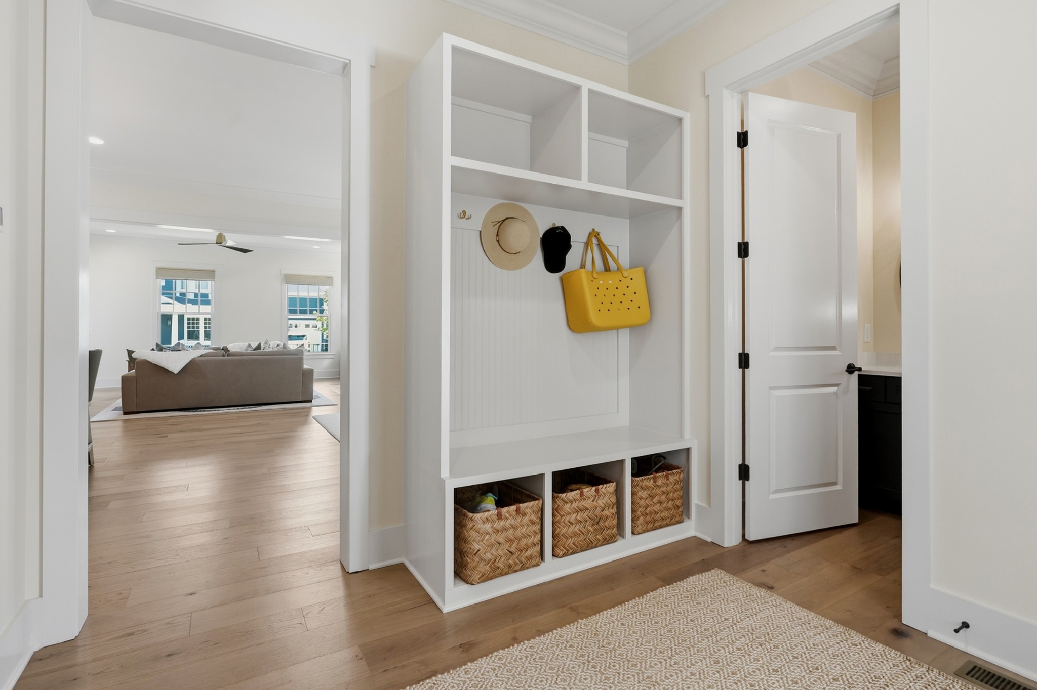 Mudroom with white built-in cubbies, woven baskets, and a yellow tote hanging from a hook.