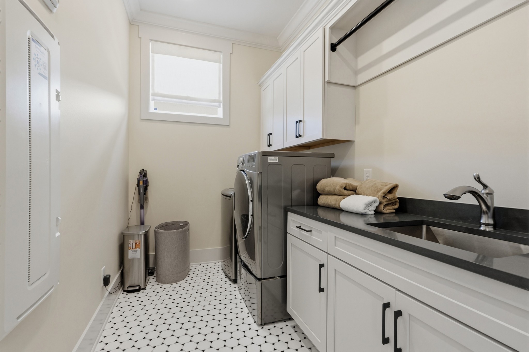 Laundry room with front-loading washer and dryer, white cabinets, black countertop, and patterned tile floor.