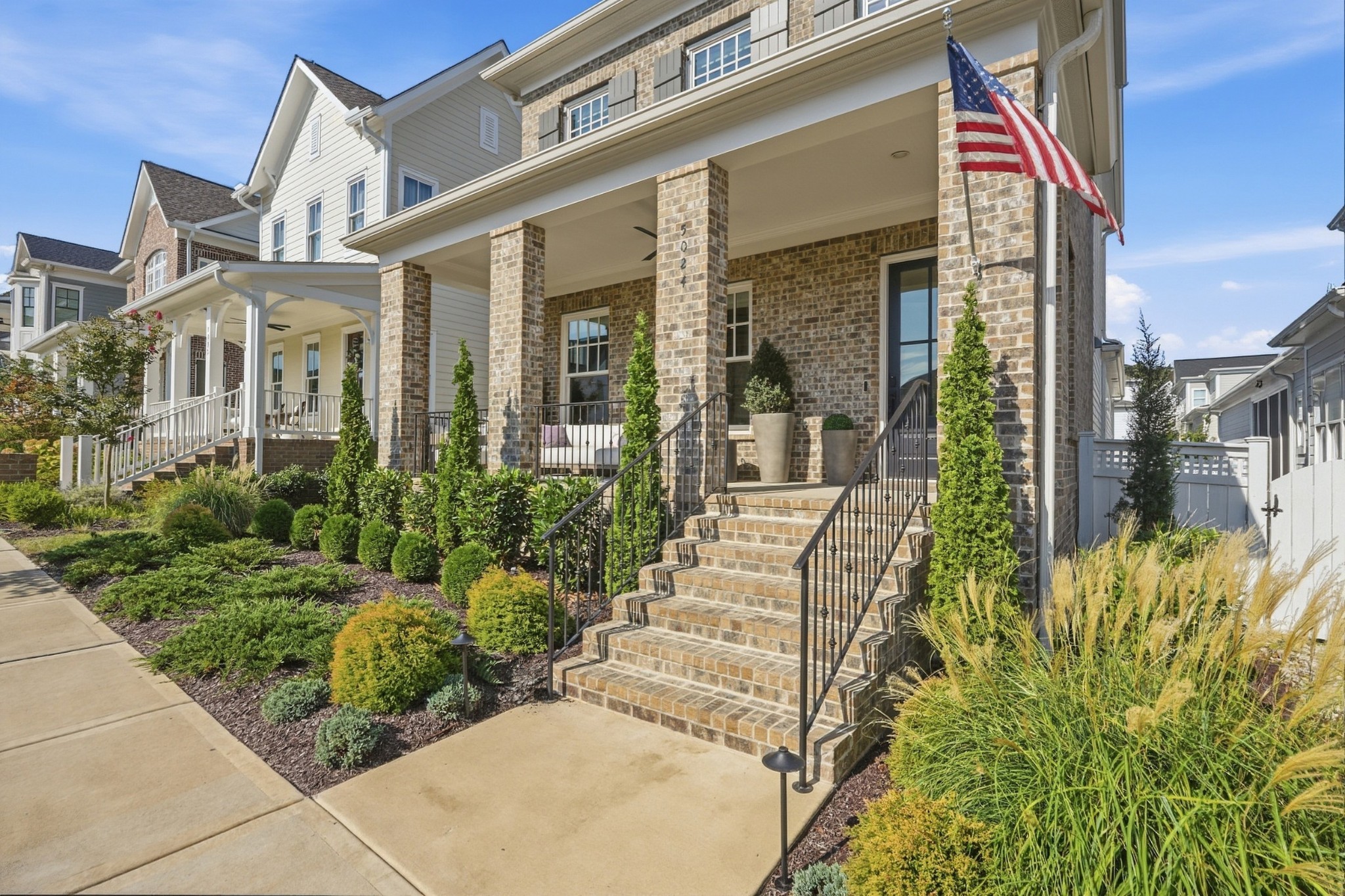 Home exterior with a covered brick porch, landscaped garden, and American flag.