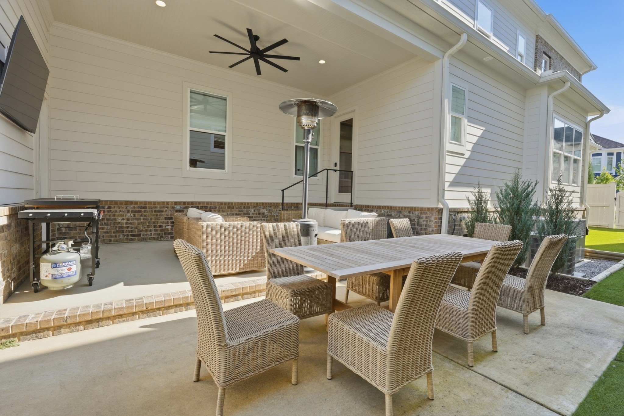 Covered patio with wicker dining furniture, lounge seating, a ceiling fan, and a gas grill.