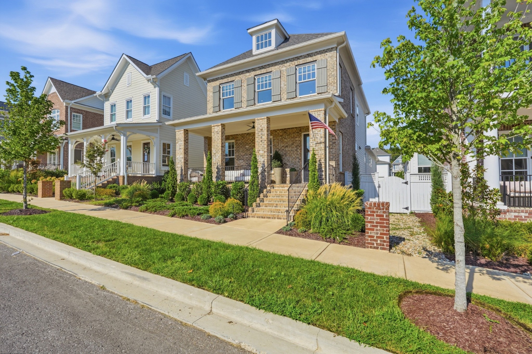 Two-story brick-and-siding house with a covered porch, landscaped front garden, and American flag.