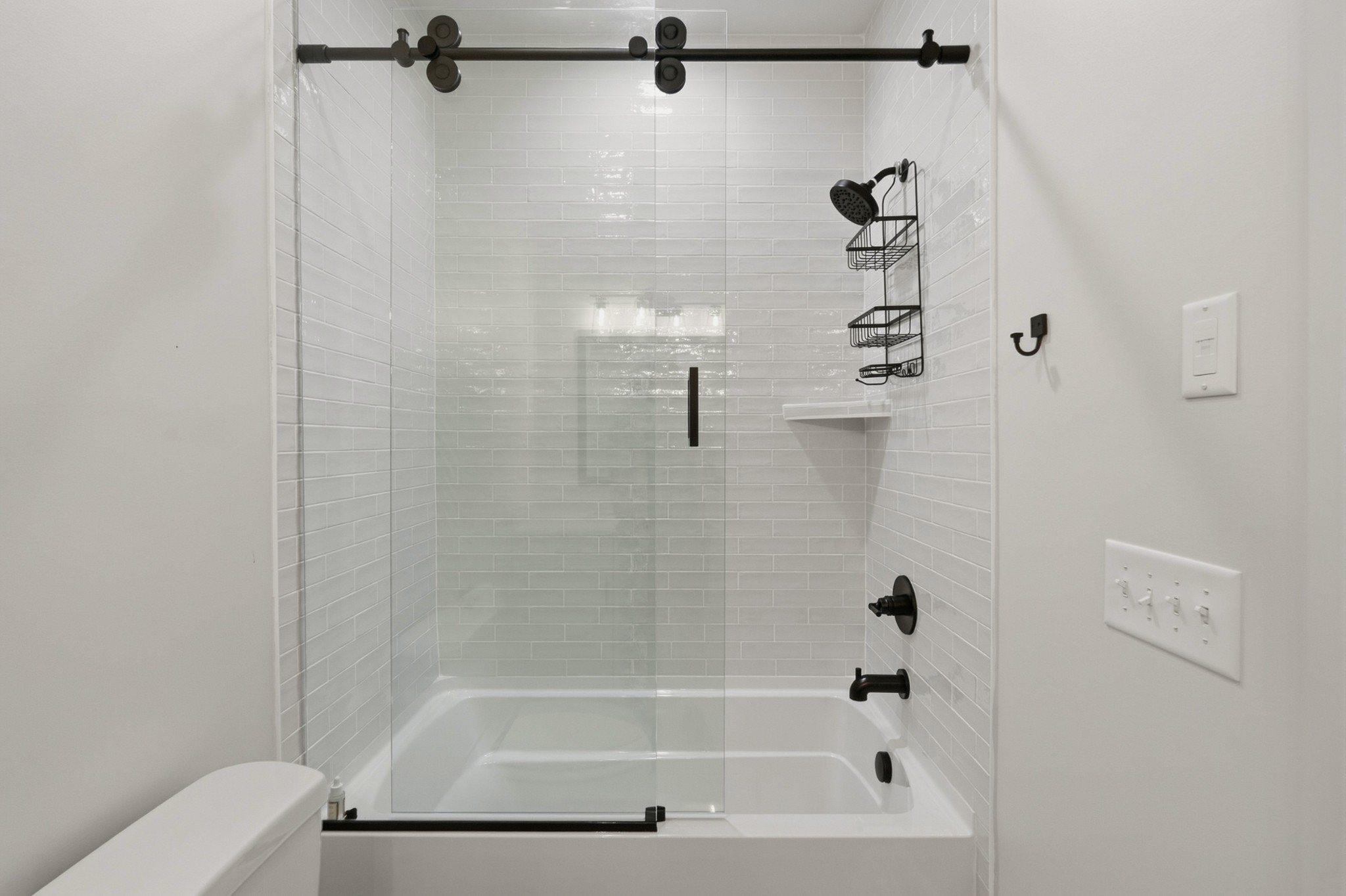 Bathroom tub and shower with glossy white subway tile, clear glass doors, and matte black fixtures.