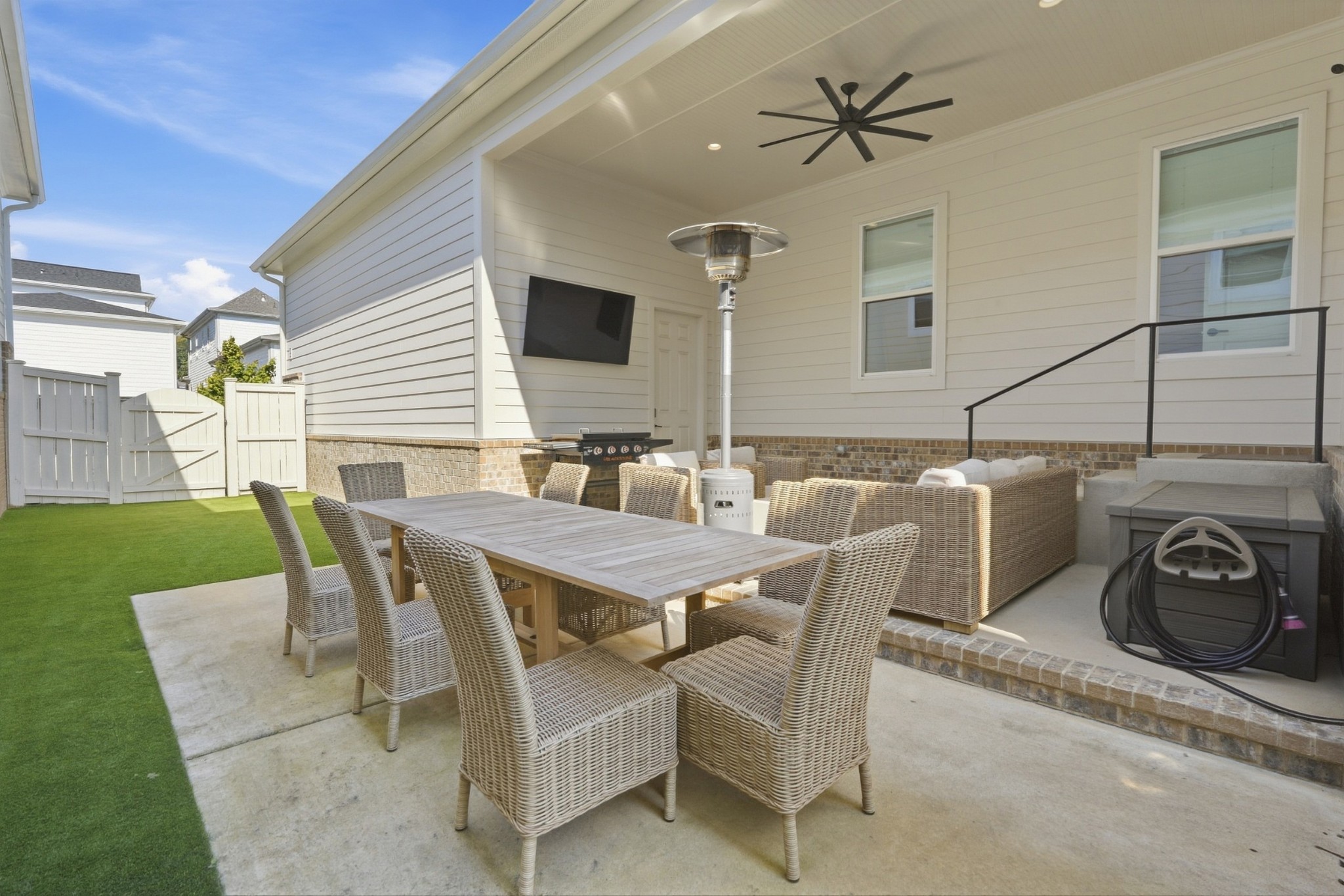 Covered backyard patio with wicker dining and lounge seating, a ceiling fan, and outdoor heater.