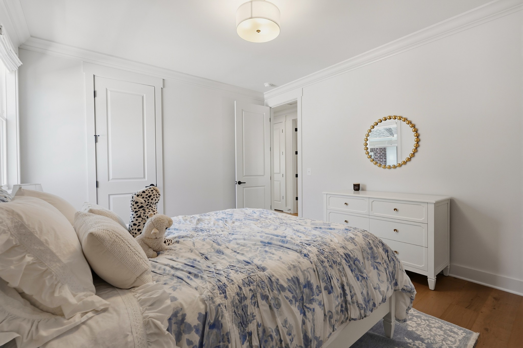 Bedroom with blue floral bedding, a white dresser, and a round gold-beaded mirror.