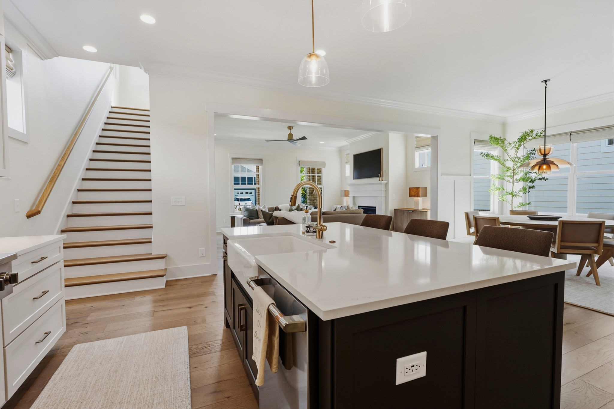 Open-plan kitchen with a large dark island, white countertops, brass faucet, and staircase beside the living area.
