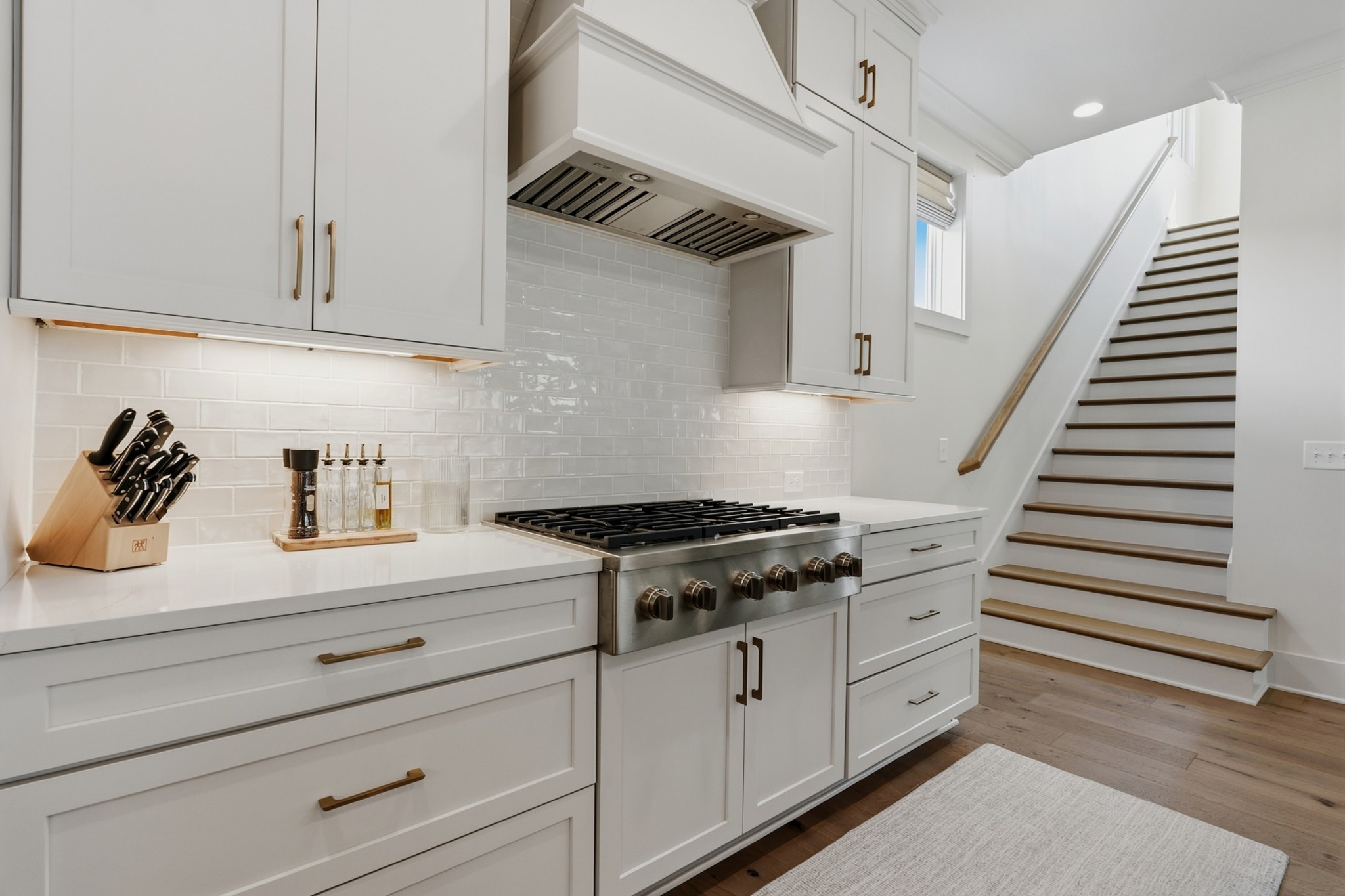 White kitchen with a stainless steel range and staircase with wood treads.