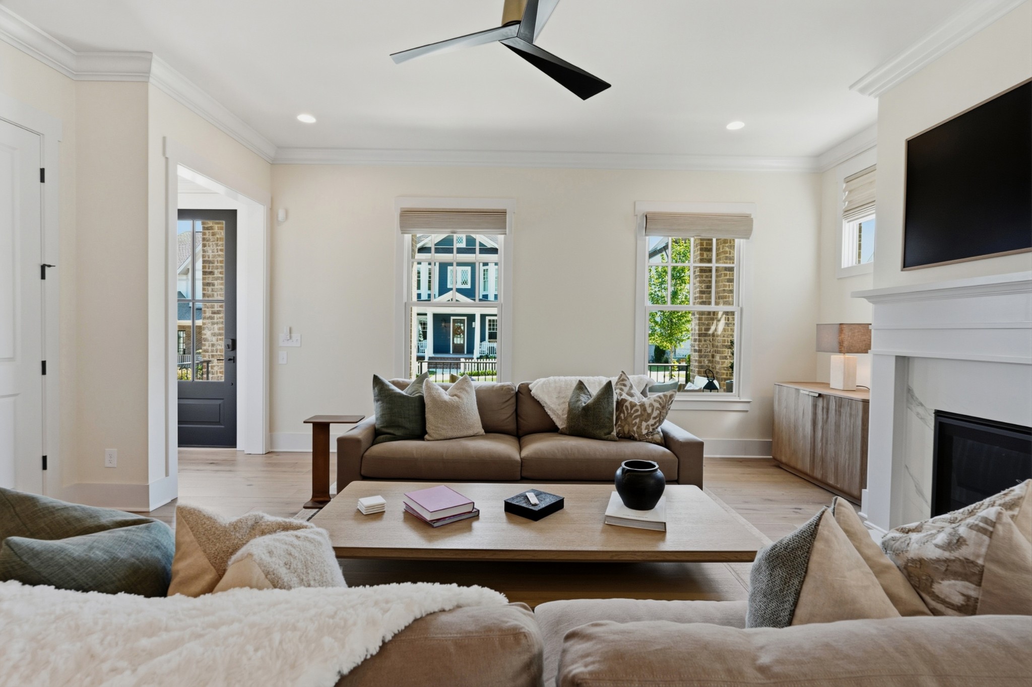 Furnished living room with large windows, neutral seating, and a fireplace.