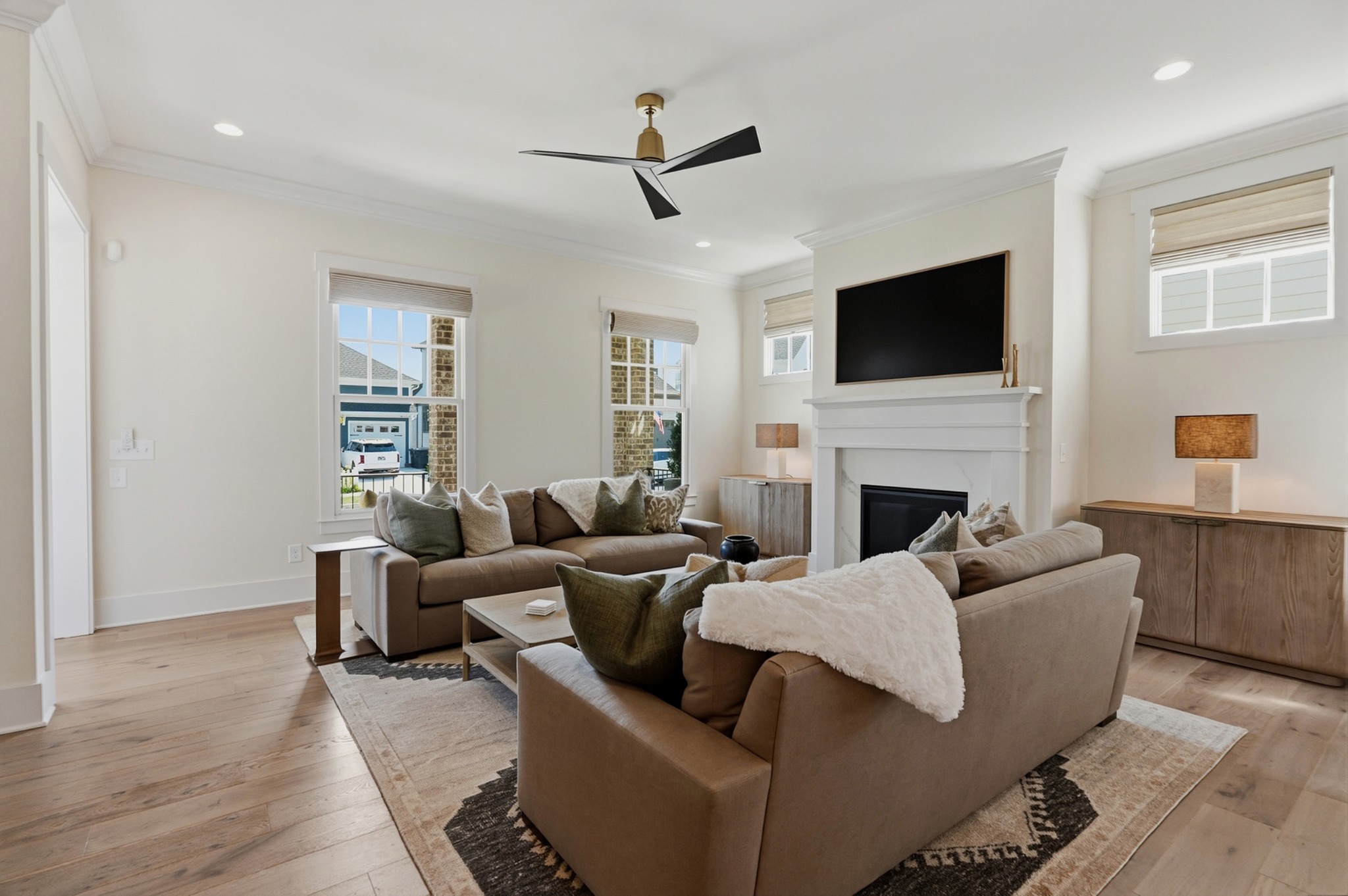 Living room with taupe sofas facing a white fireplace and television, large windows, and wood floors.