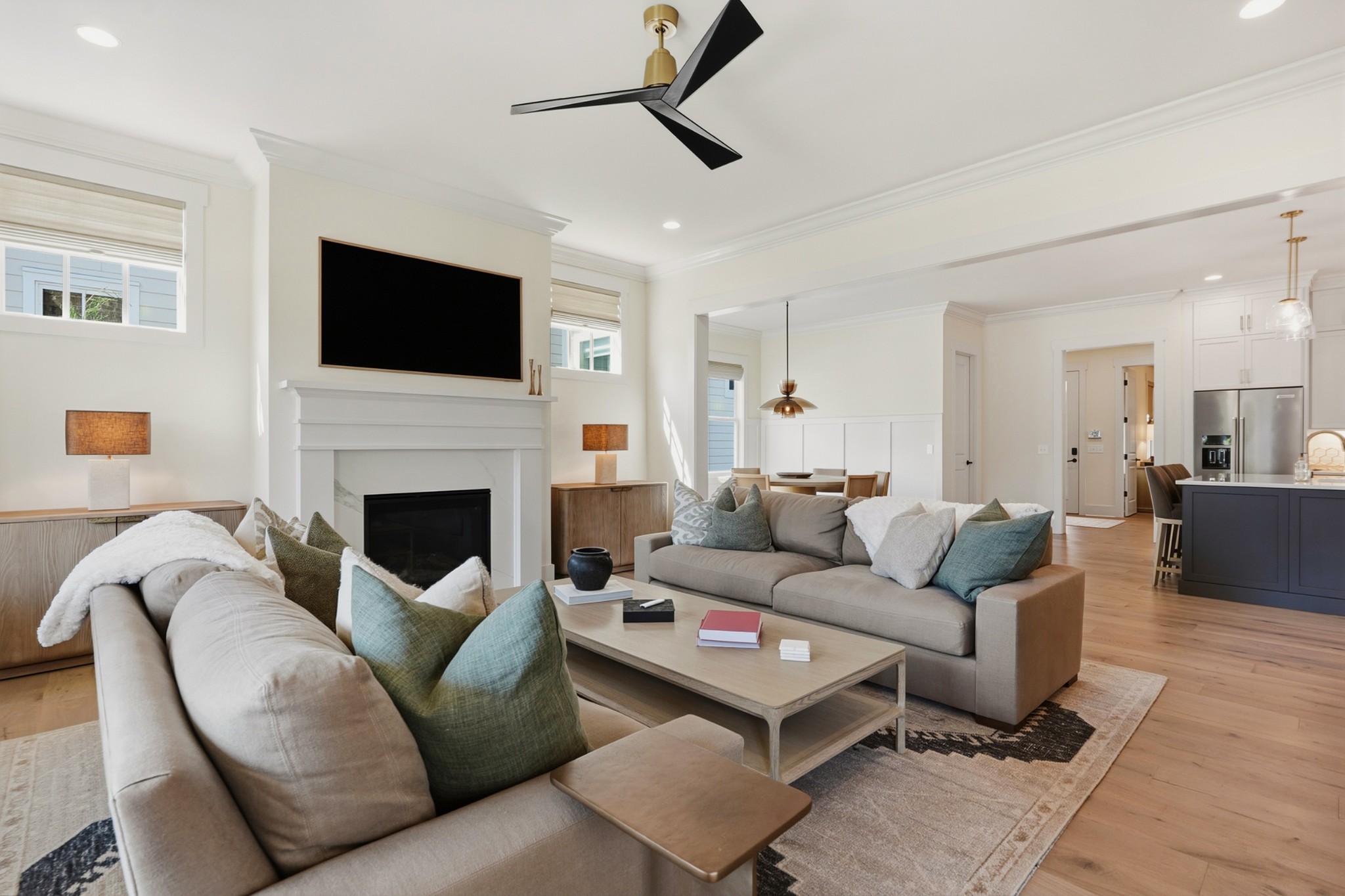 Staged living room with a white fireplace, gray sofas, and open dining and kitchen areas.