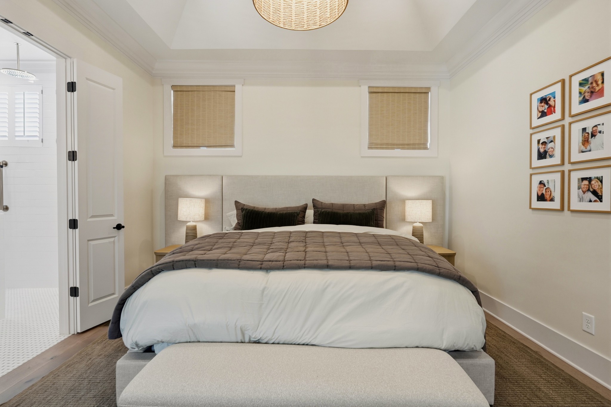 Staged bedroom with a large bed, matching bedside lamps, and an open doorway to a tiled bathroom.