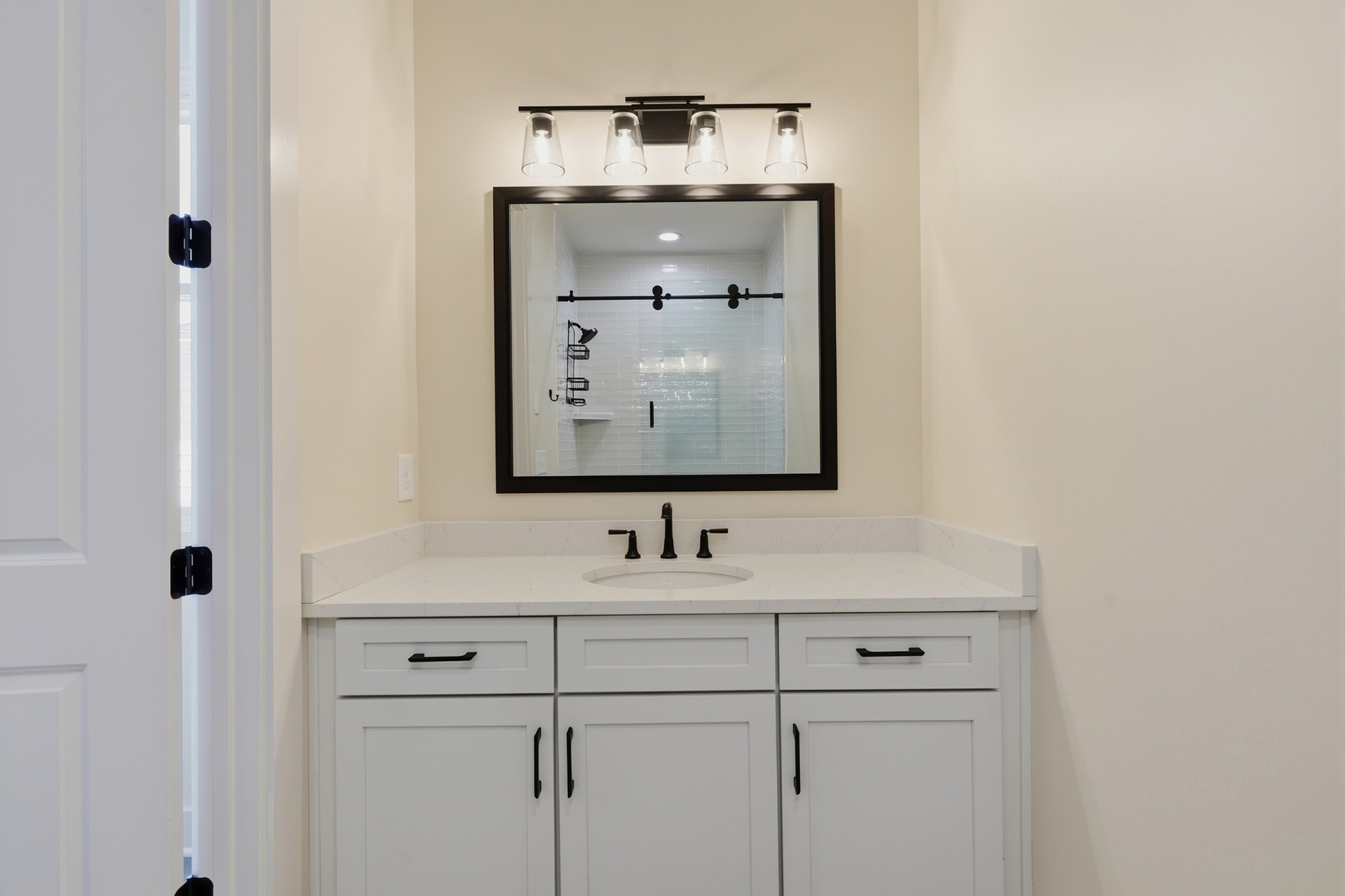 Bathroom vanity with a black-framed mirror reflecting a white-tiled shower and black sliding door rail.