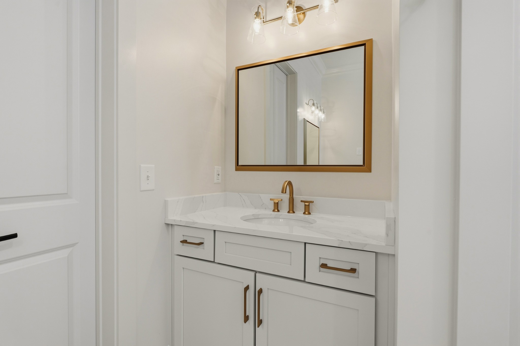 Bathroom vanity with a marble-look counter, brass fixtures, white cabinetry, and a large framed mirror.