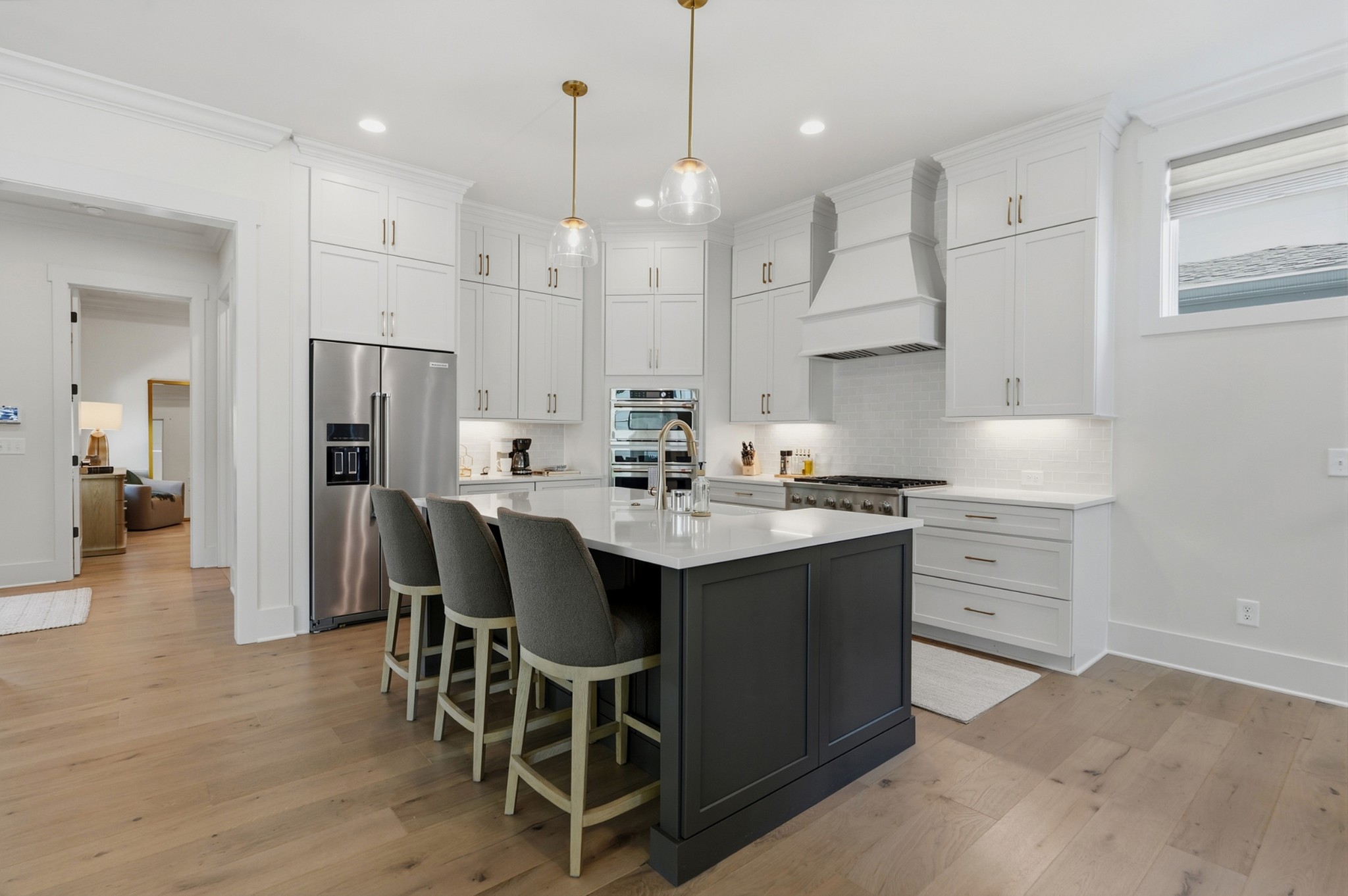 Modern kitchen with a dark island, three stools, white cabinets, and stainless steel appliances.