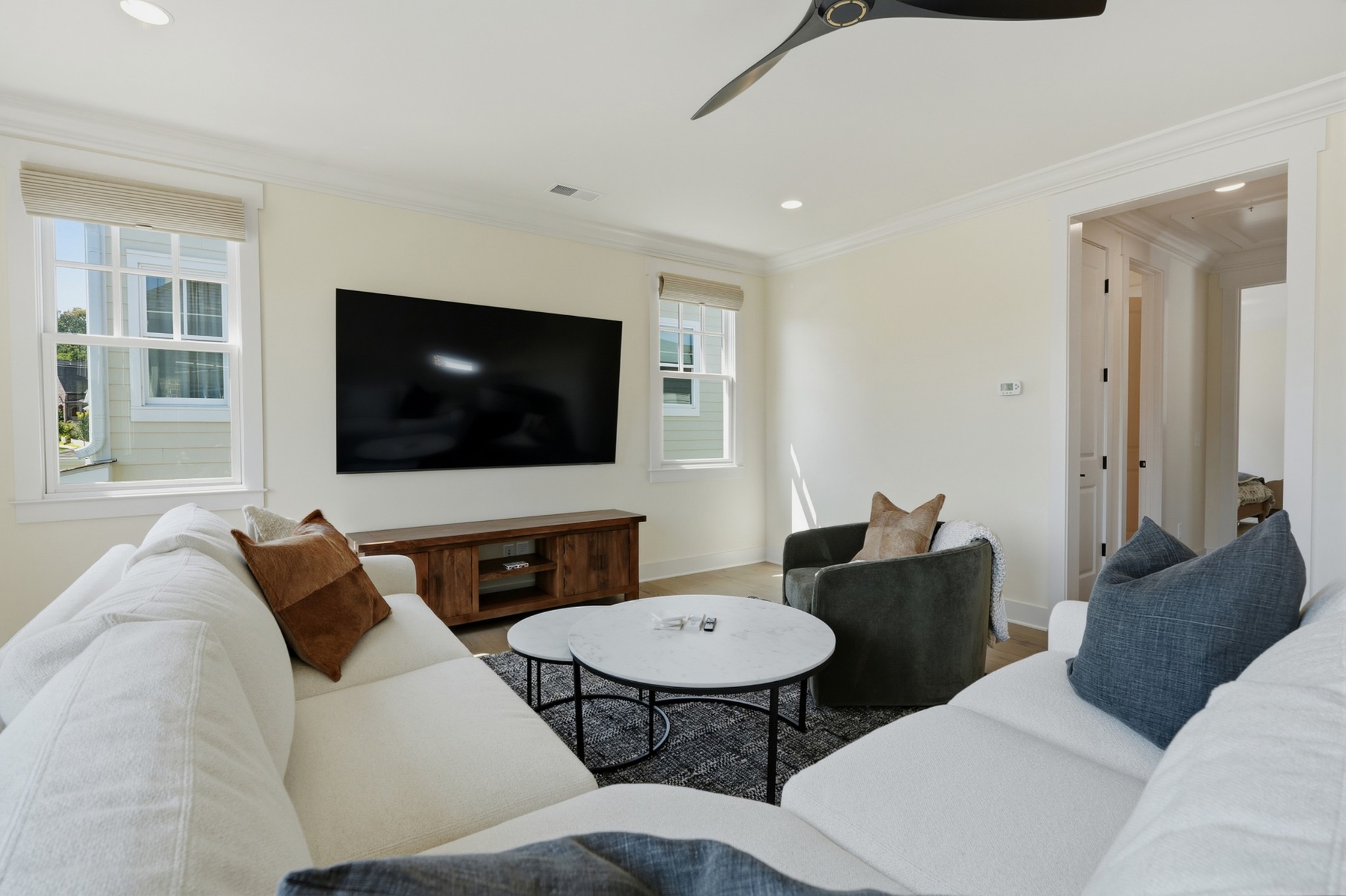Living room with white sofas, a green armchair, round coffee tables, and a wall-mounted television.