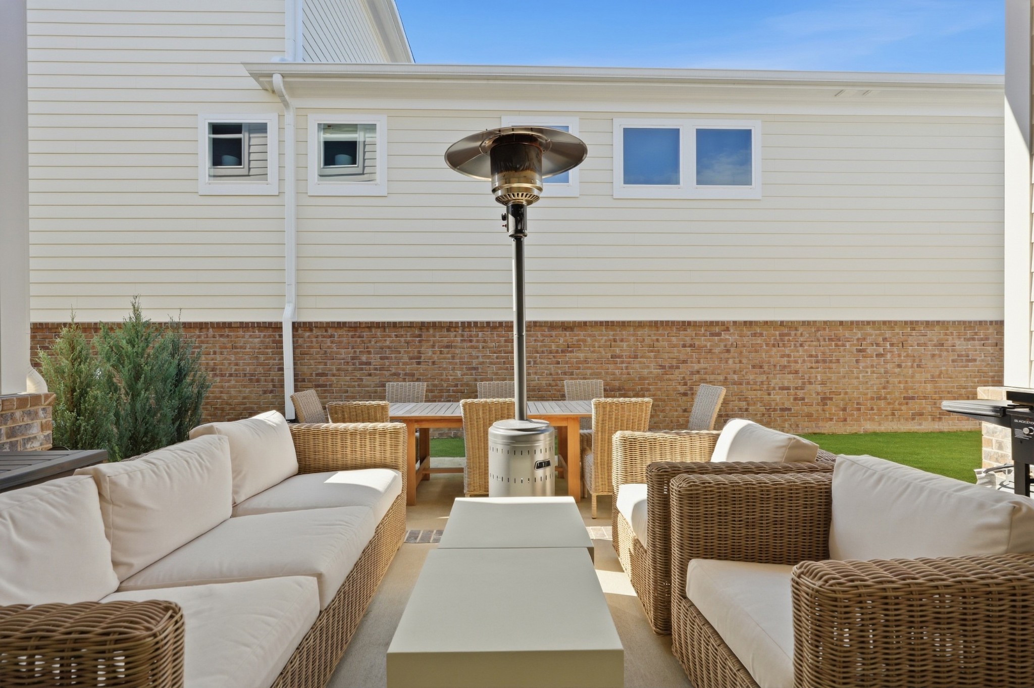 Outdoor patio with wicker seating, dining table, and a tall freestanding heater beside the house.