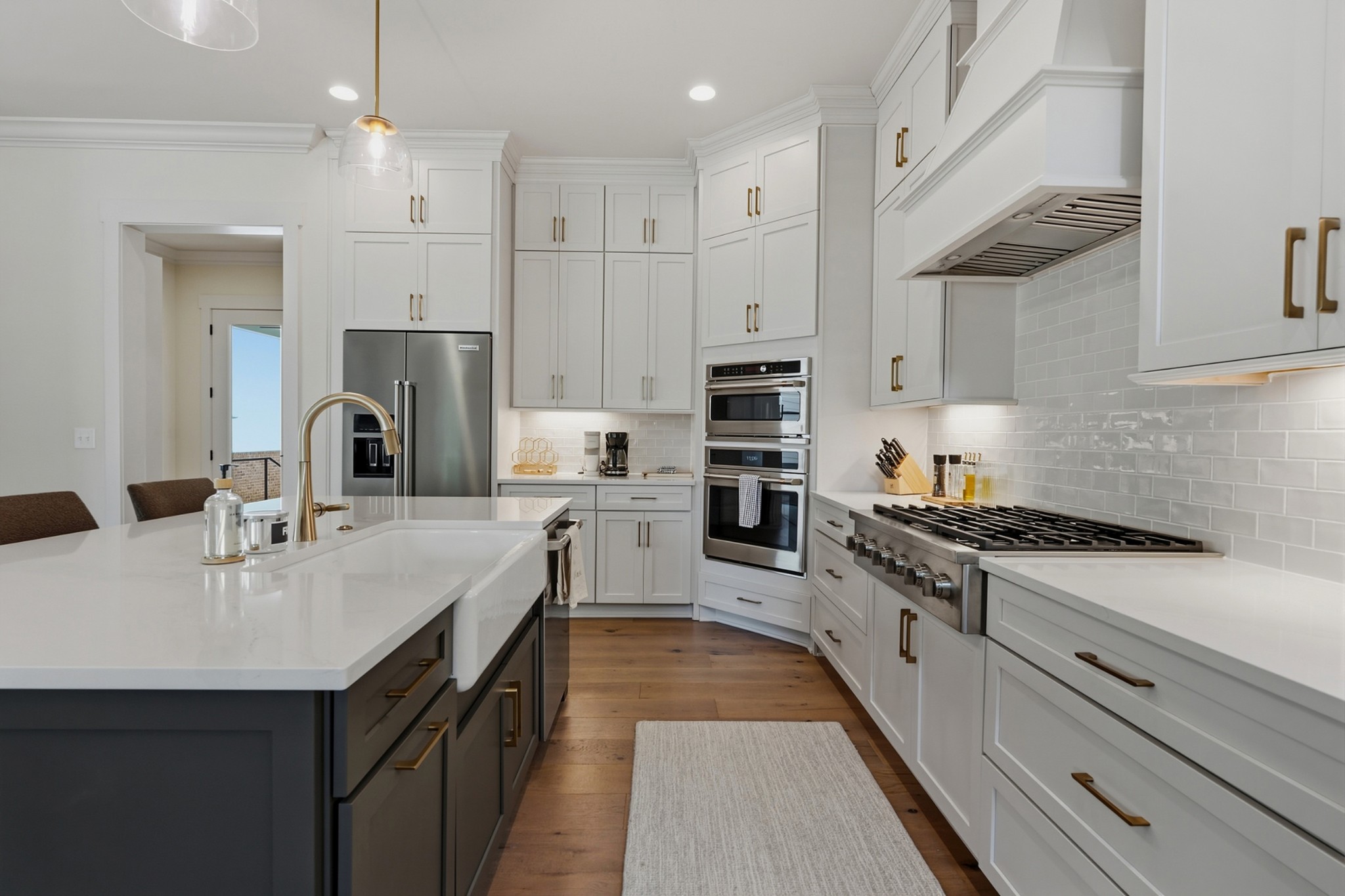 Kitchen with white cabinetry, brass hardware, stainless steel appliances, and a large dark island.