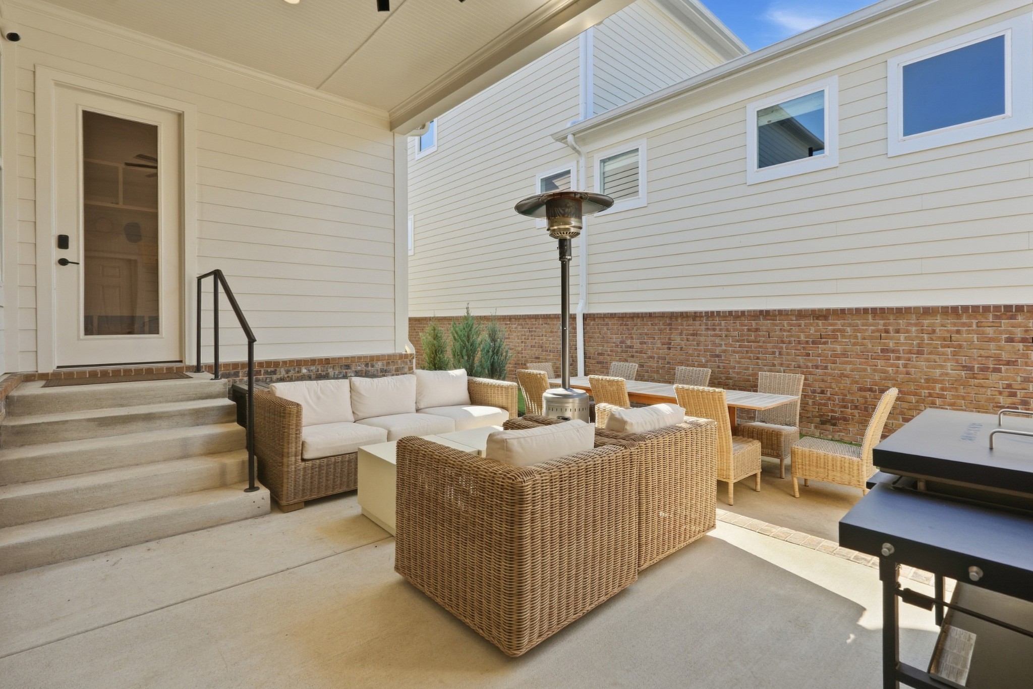 Furnished patio with wicker seating, a dining set, patio heater, and grill beside the house.