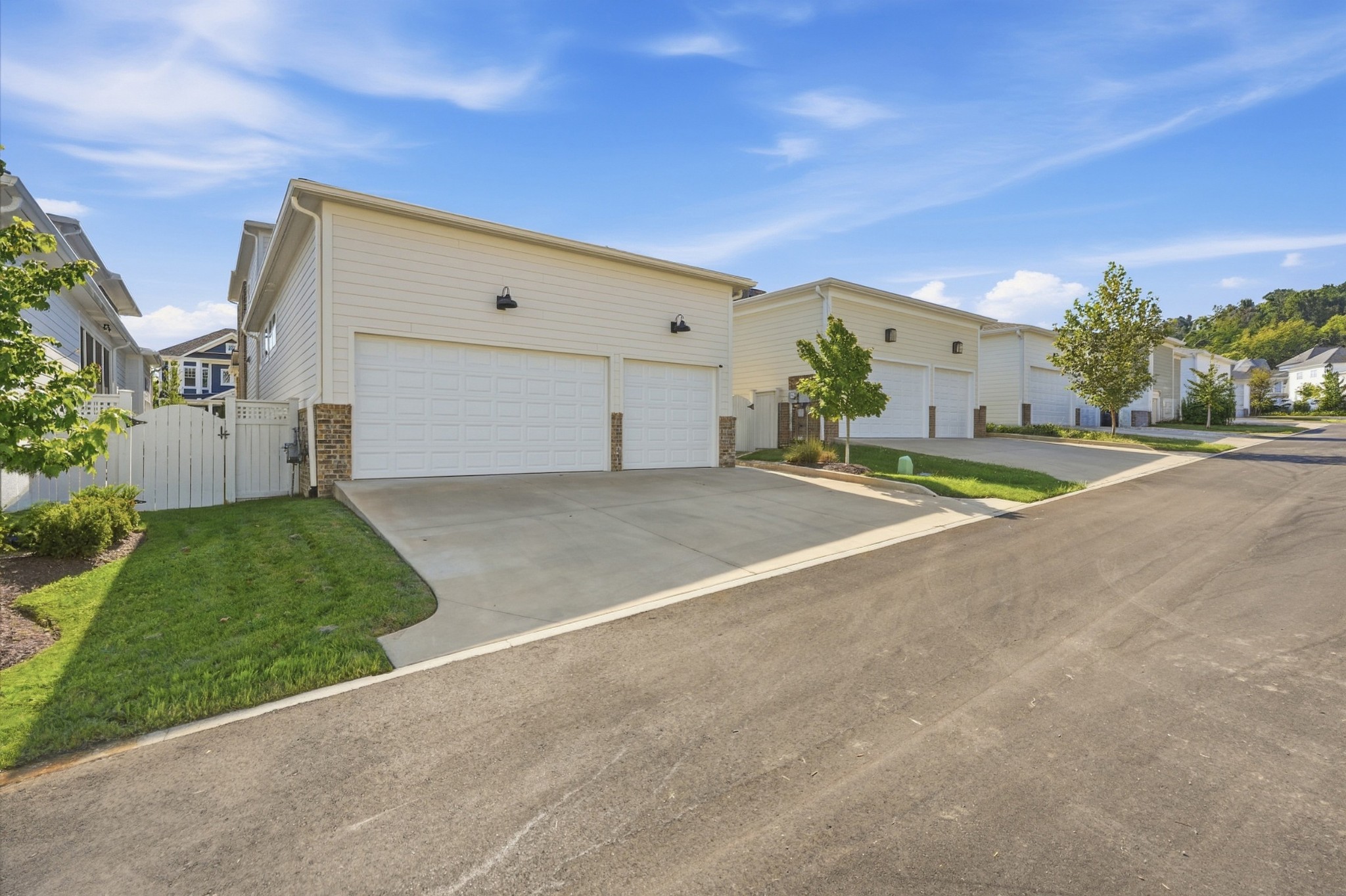 Light-sided home with white garage doors, a wide driveway, and a white fence.