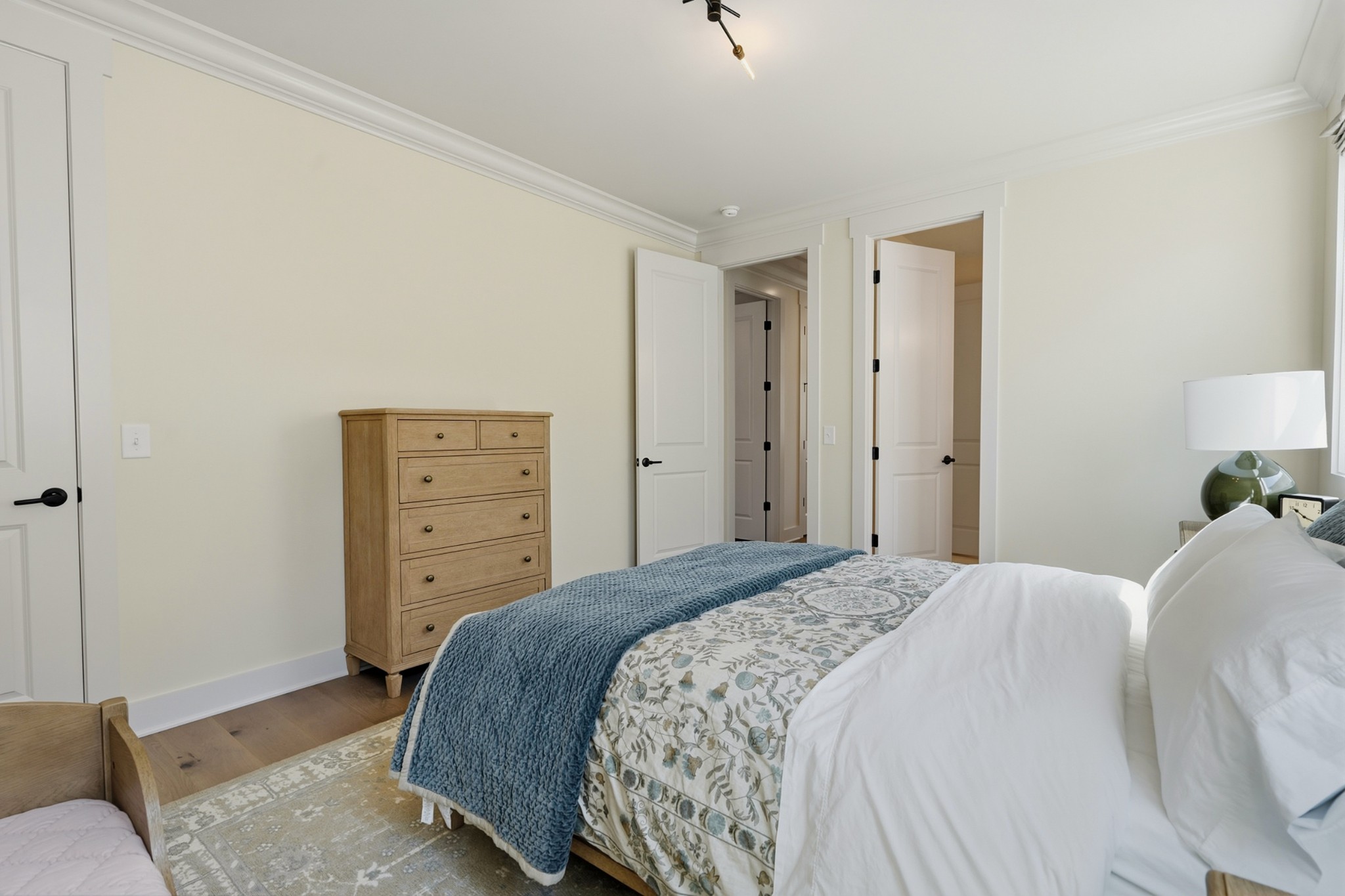 Bedroom with a blue throw over a floral bedspread and a tall wooden chest of drawers.