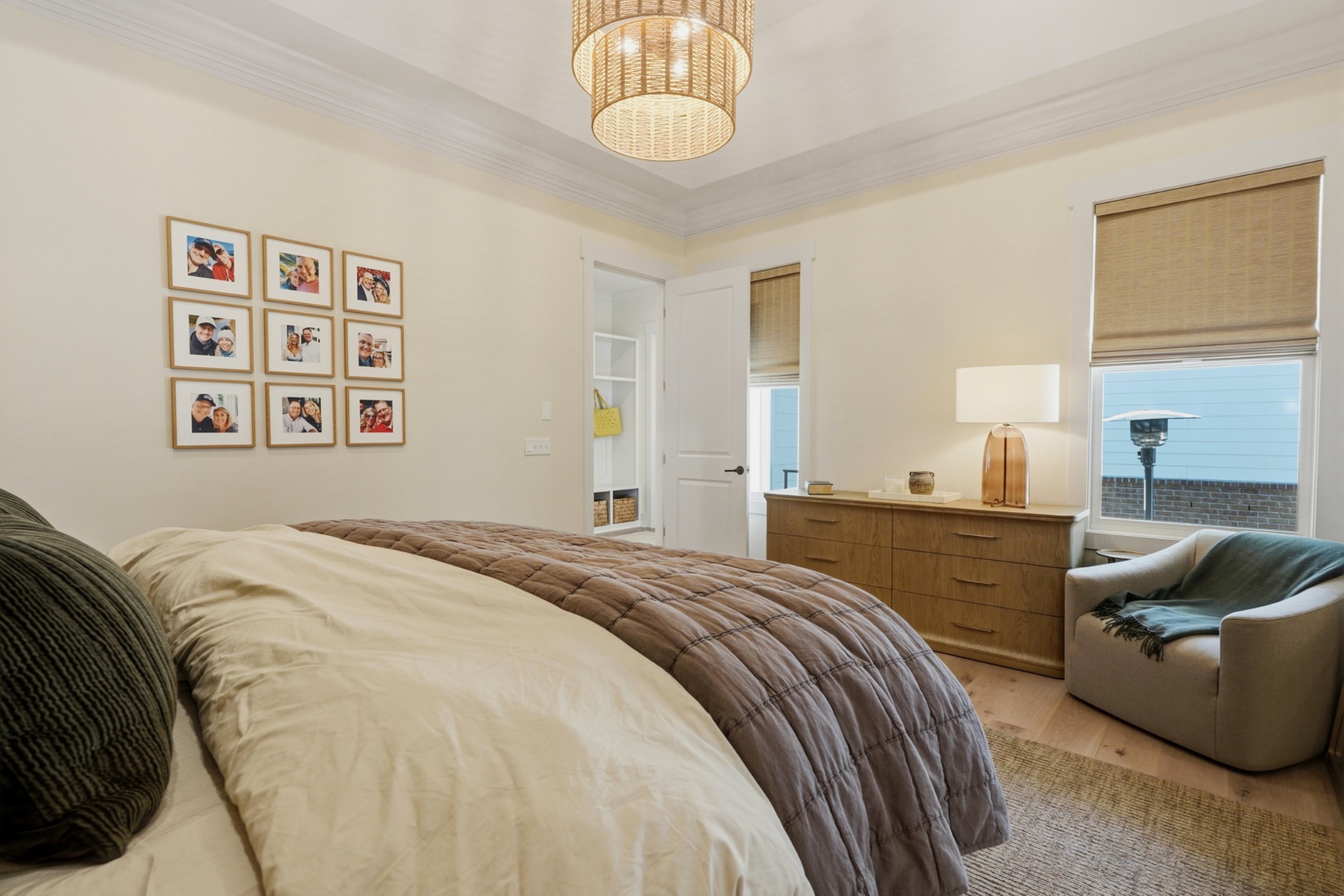 Furnished bedroom with a large bed, framed photo gallery, wood dresser, and window-side armchair.