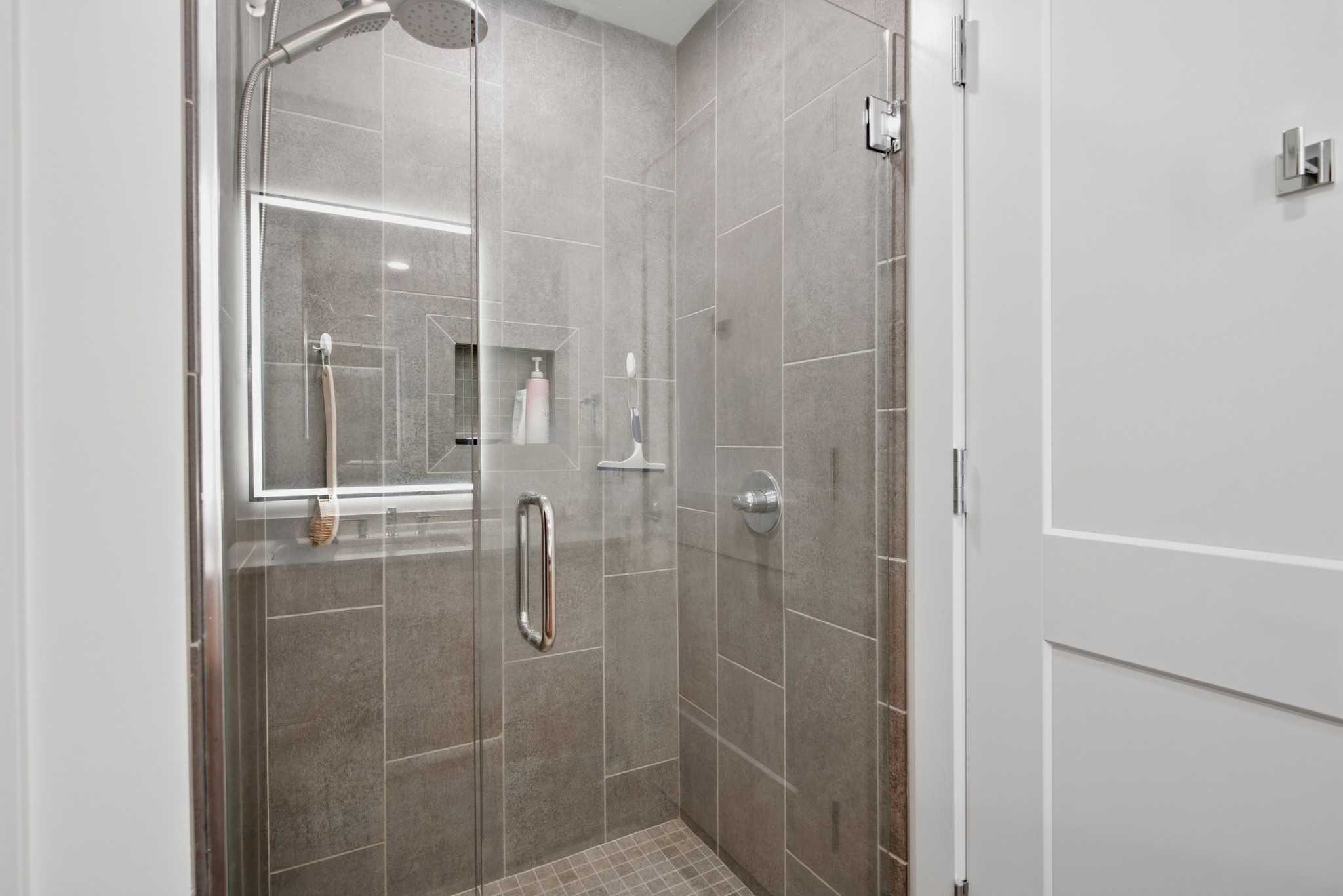 Walk-in shower with gray tile, glass enclosure, rainfall showerhead, and recessed toiletries niche.