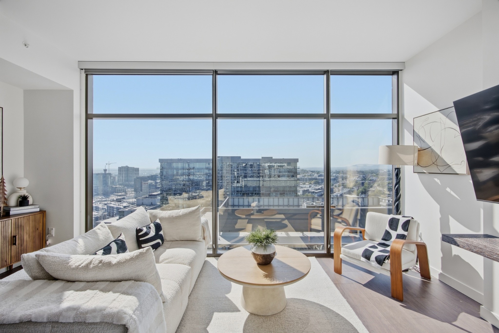 High-rise living room with floor-to-ceiling windows, white furnishings, and a city skyline view.