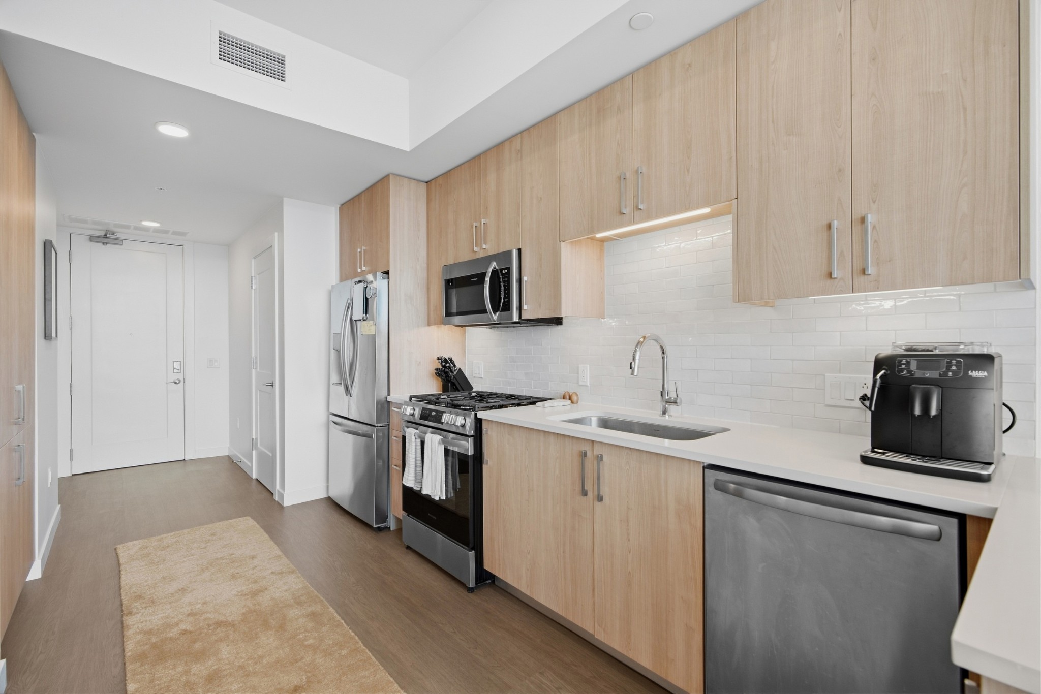 Modern condo kitchen with light wood cabinets, stainless steel appliances, and a white subway tile backsplash.