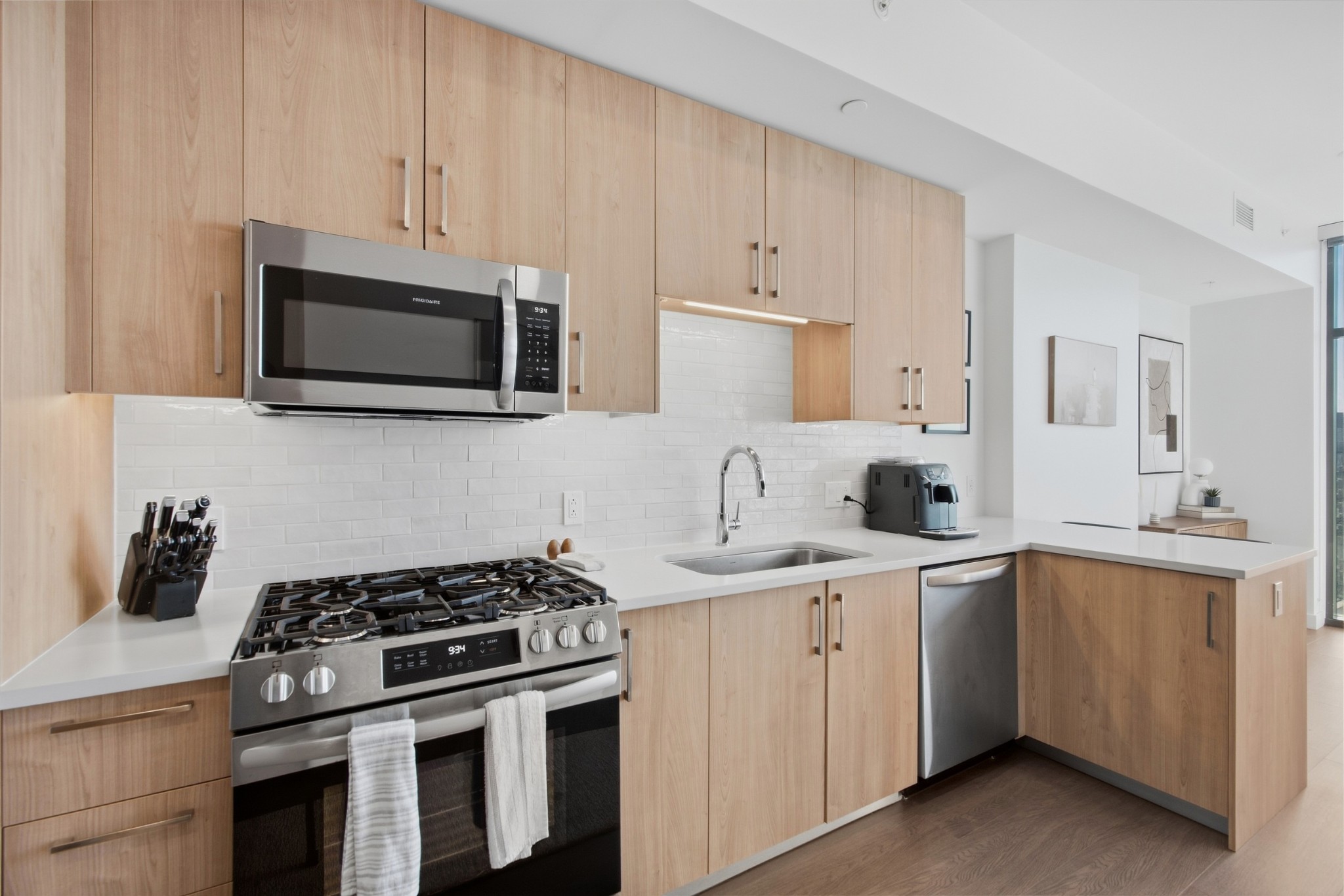 Modern condo kitchen with light wood cabinets, stainless appliances, white tile backsplash, and a breakfast bar.