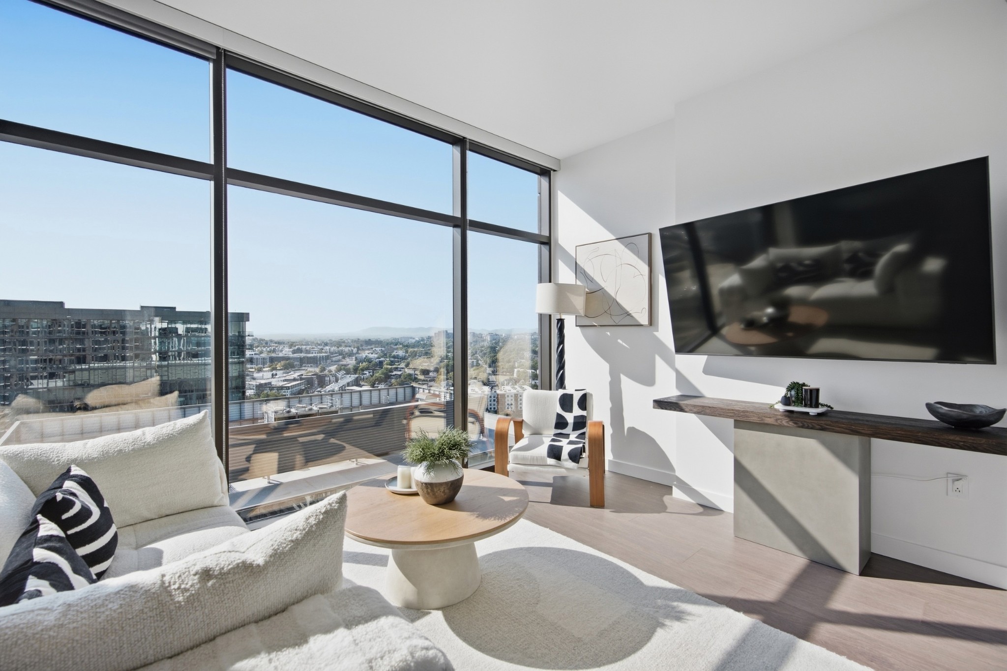High-rise condo living room with floor-to-ceiling windows overlooking downtown buildings and distant hills.