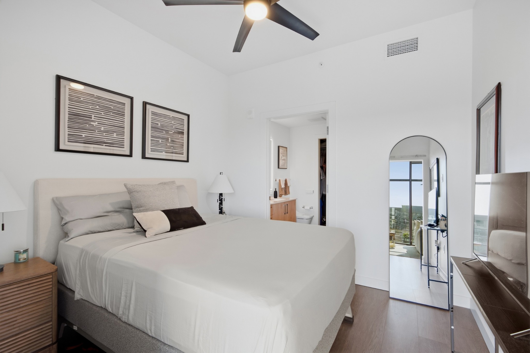 Furnished bedroom with a white bed, arched mirror, and bathroom doorway.