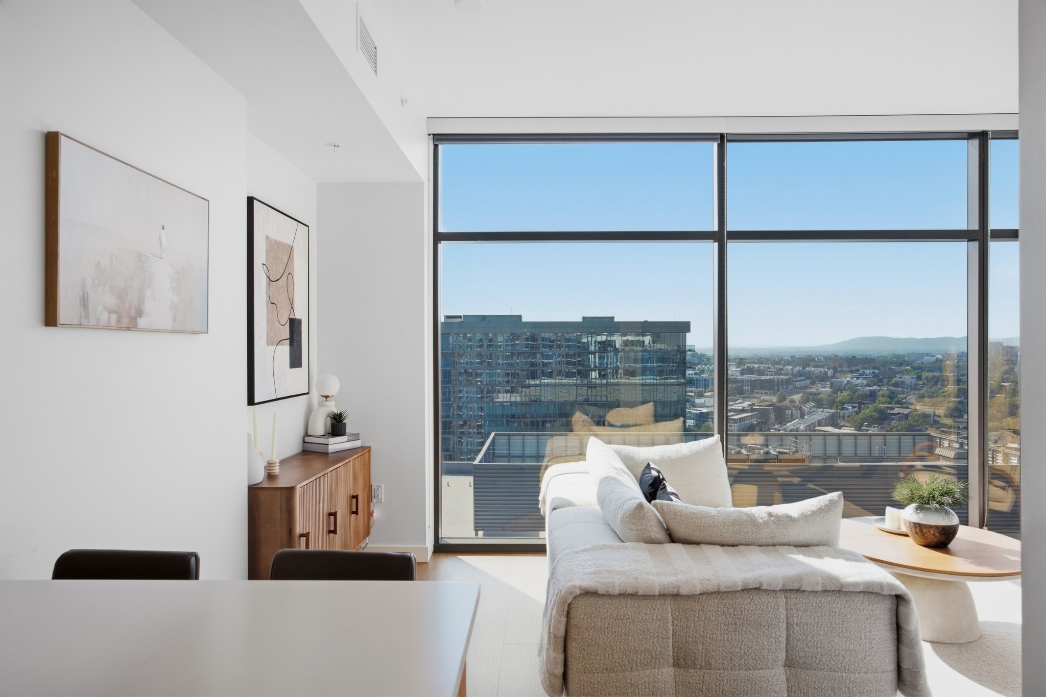 Furnished condo living room with a white sectional and floor-to-ceiling city-view windows.