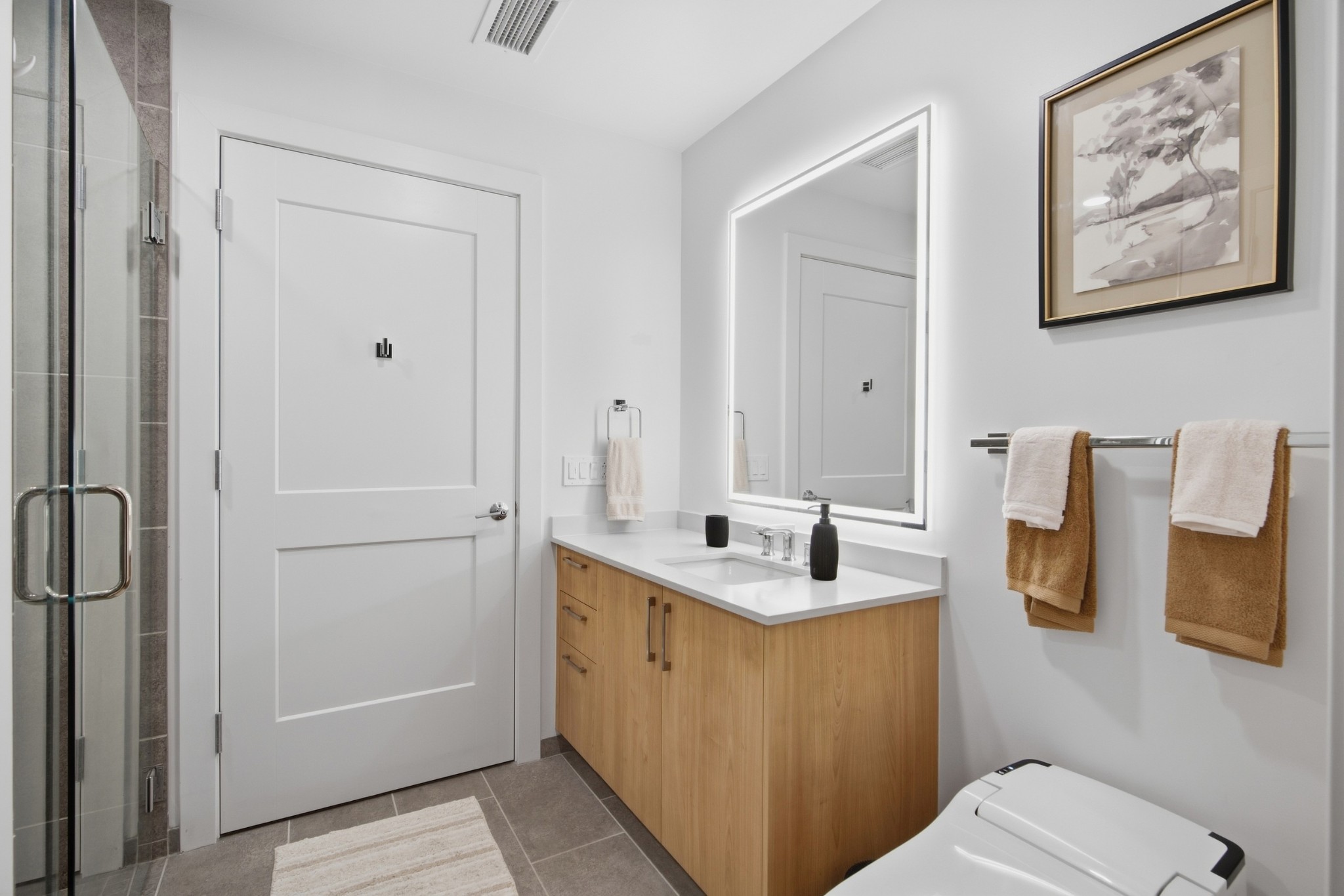 Modern bathroom with a wood vanity, illuminated mirror, glass shower, and bidet toilet.