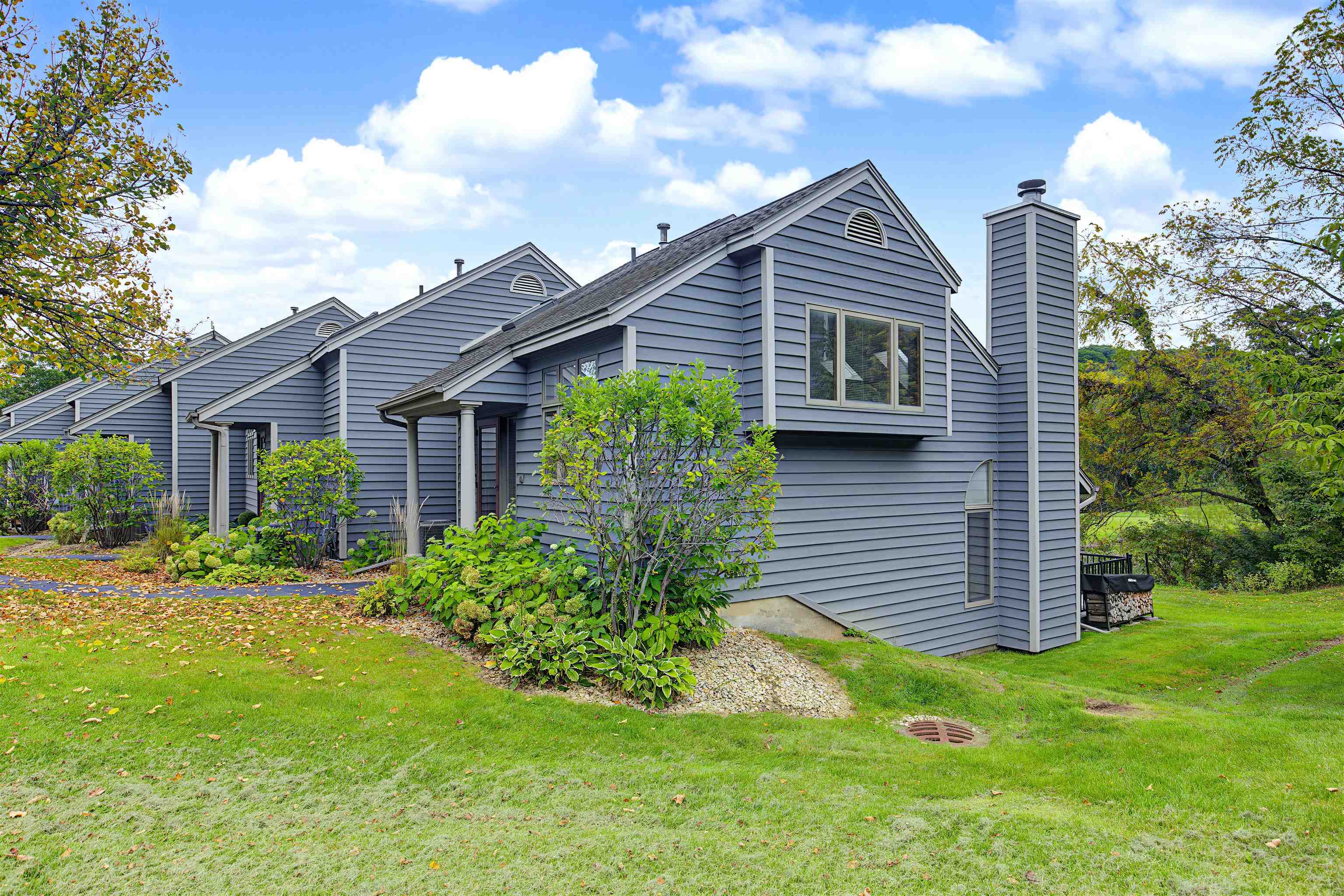 Gray-blue homes with pitched roofs and white trim beside a landscaped lawn.