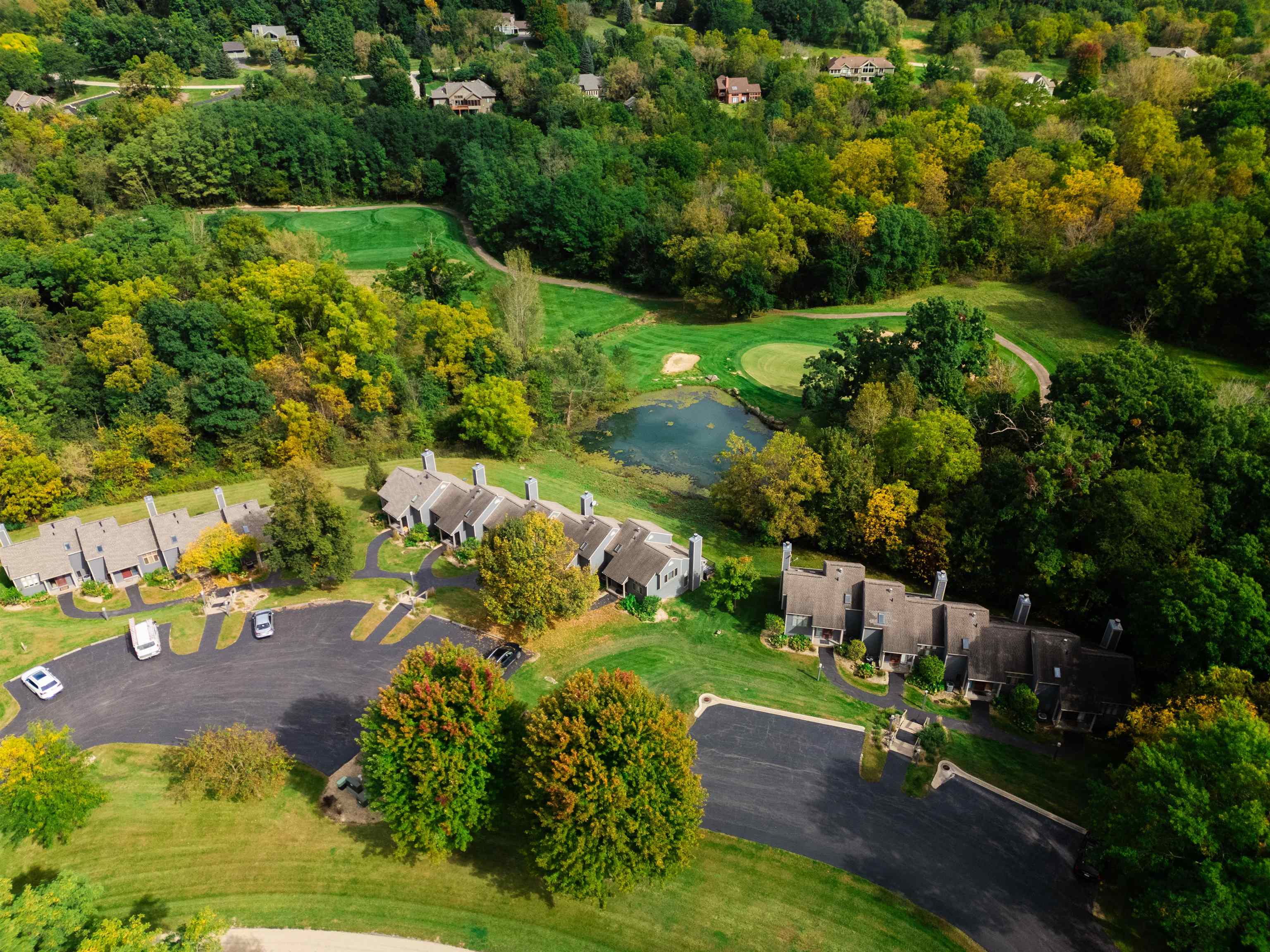 Aerial view of attached homes among autumn trees beside a pond and golf green.